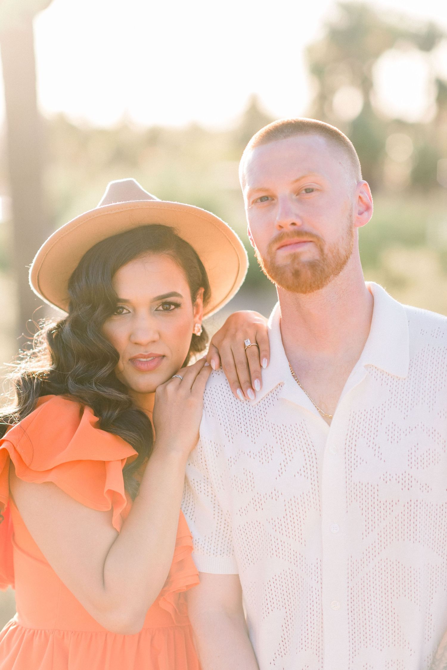 A couple poses in sunset lighting while wearing orange dress and white shirt against a desert backdrop.