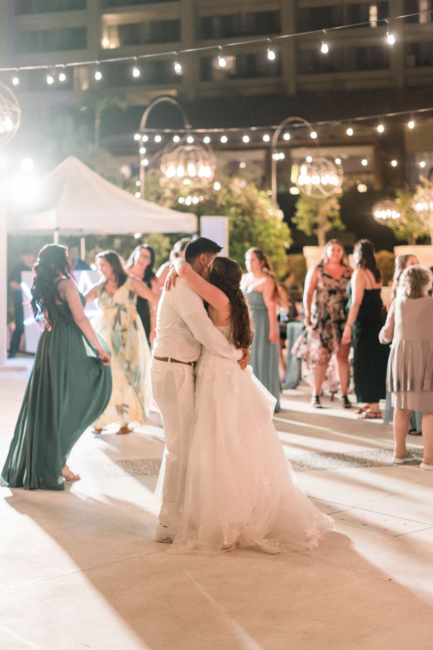 Bride and groom share intimate slow dance under string lights at outdoor reception.