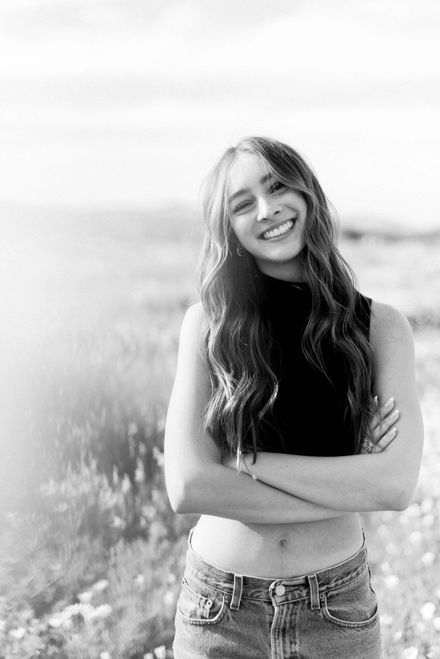 A black and white portrait showcasing casual style with a cropped top and jeans in an outdoor setting.