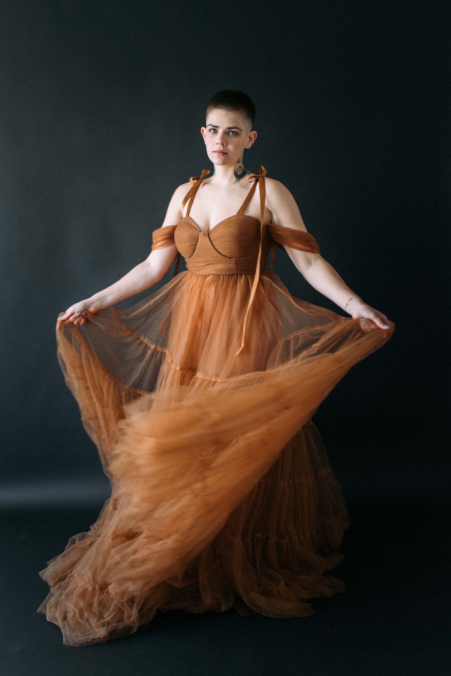 A dramatic pose showcases the movement of a brown tulle gown against a dark background.