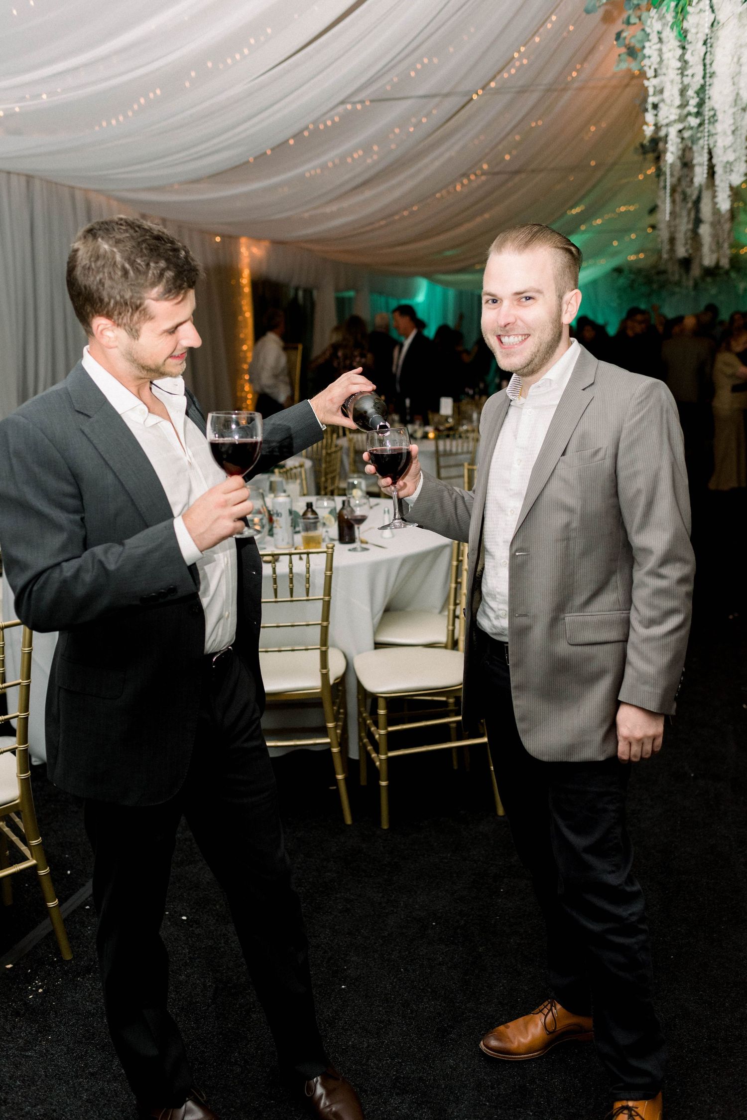 Two guests in formal attire chatting during wedding reception under decorated tent.