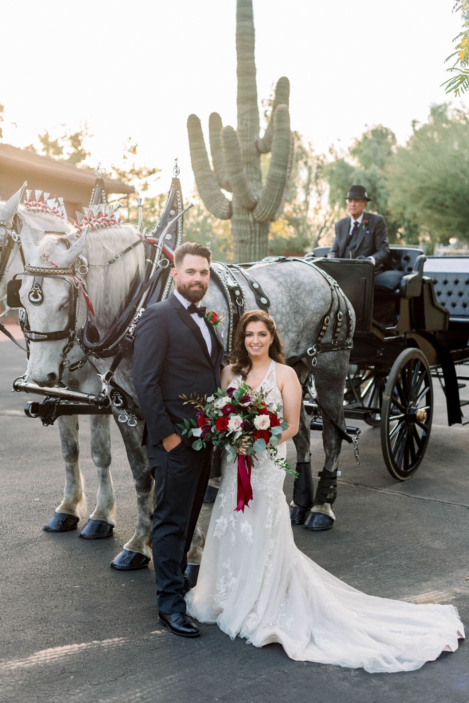 Newlyweds pose with white horse-drawn carriage and large saguaro cactus in background.