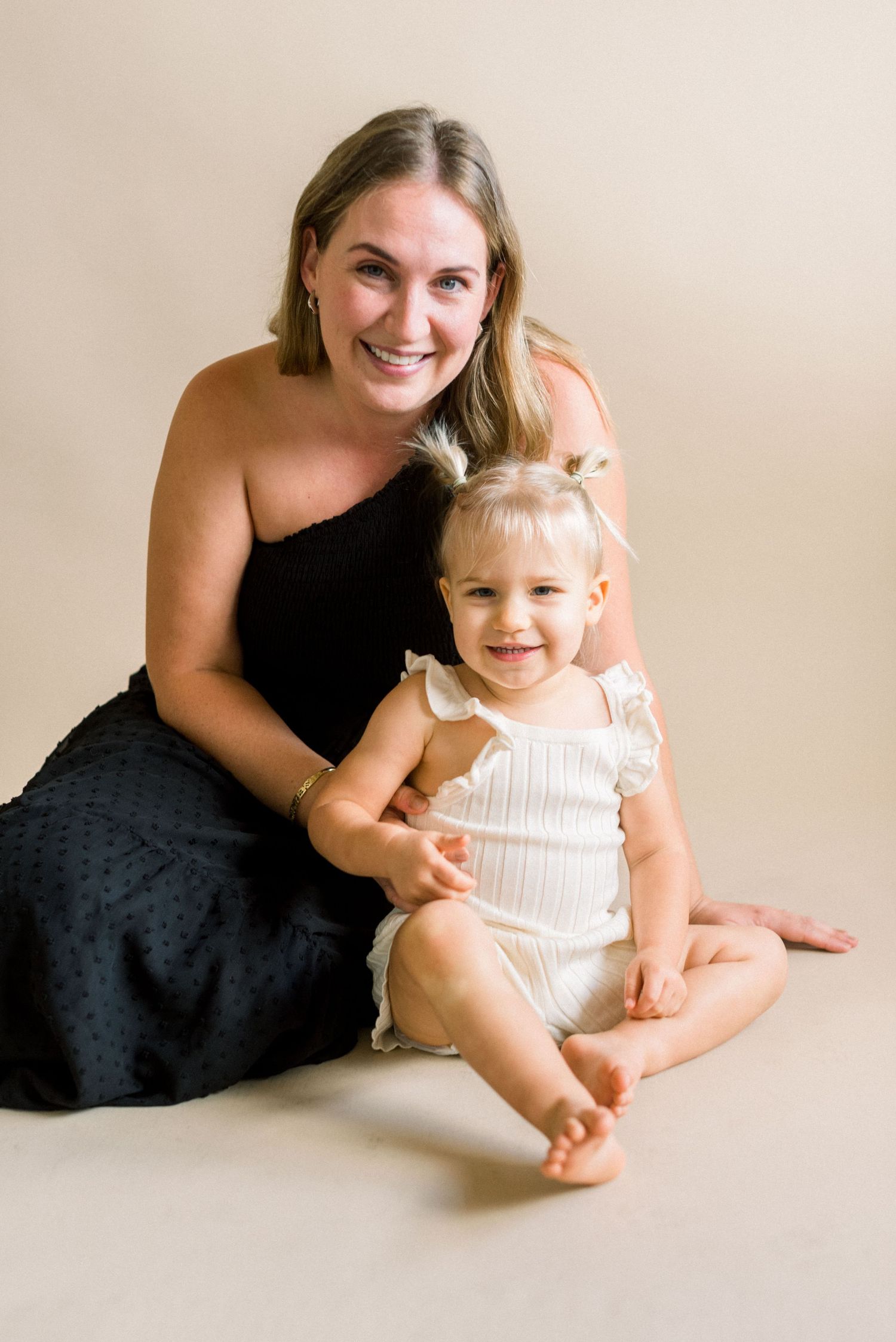 Studio portrait of two people sitting together against a neutral beige background.