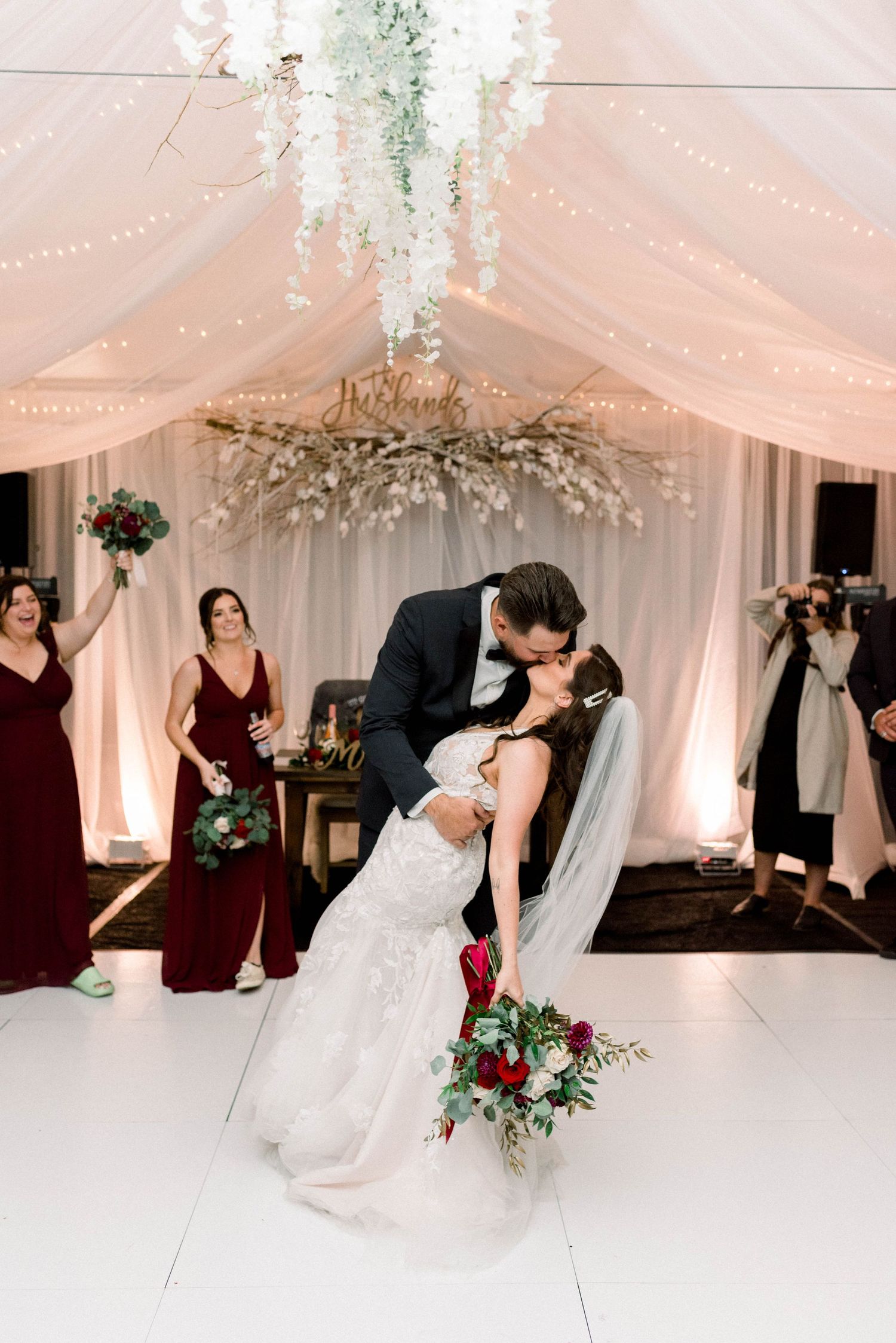 Romantic first dance moment under cascading white floral decorations and draped fabric ceiling.
