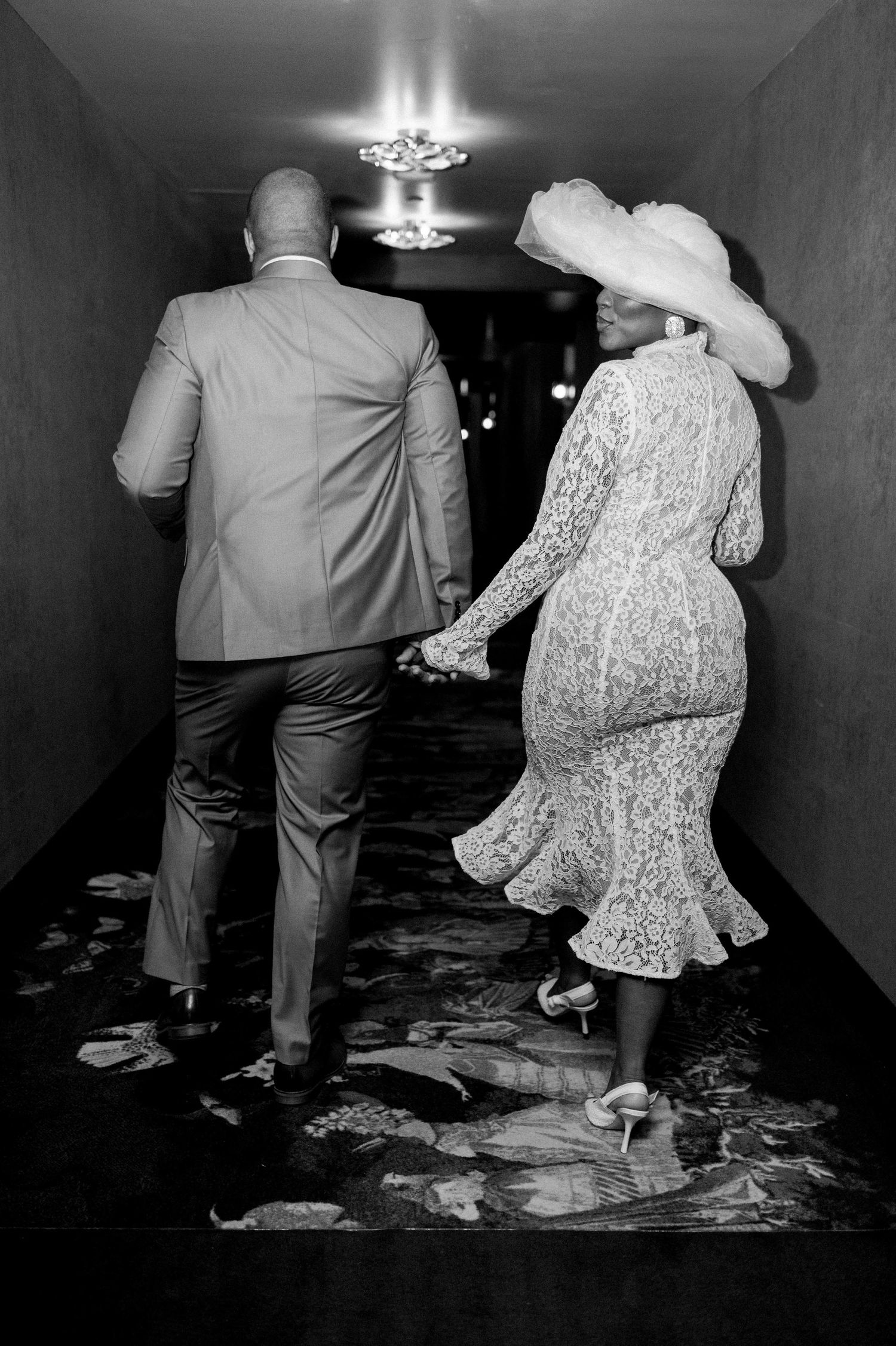 Black and white photo of newlyweds walking down a hallway together.