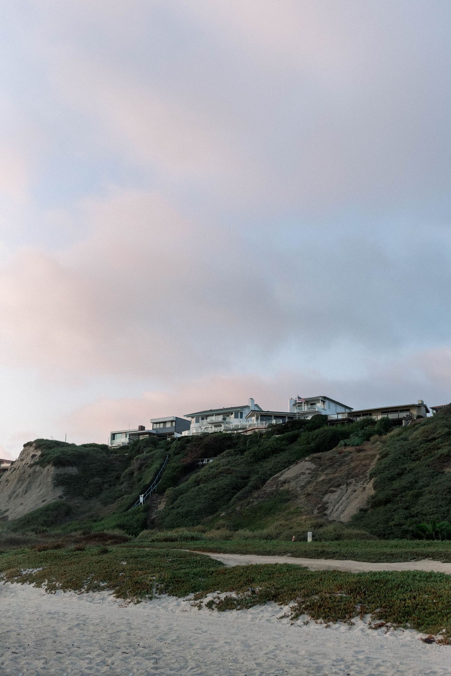 Coastal homes perched on cliffs overlooking a beach at dusk.