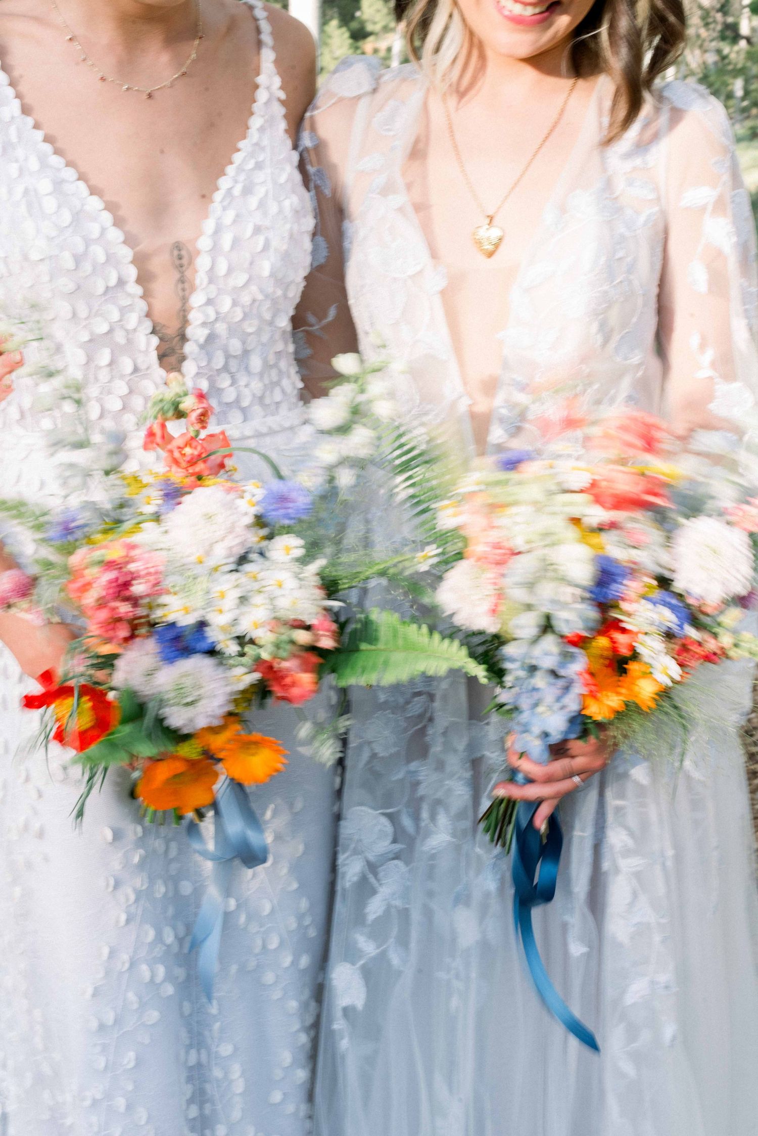 Close-up of two wedding dresses with plunging necklines and colorful bouquets featuring orange and blue flowers.