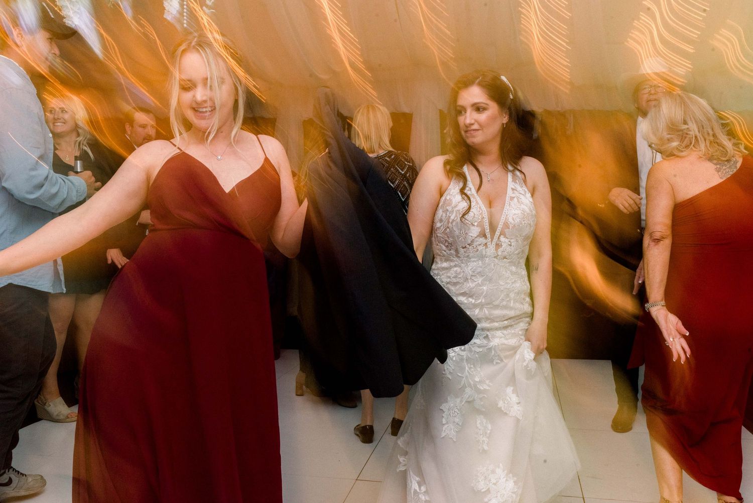 Wedding celebration on dance floor with bride in white gown and bridesmaids in red dresses dancing at reception.