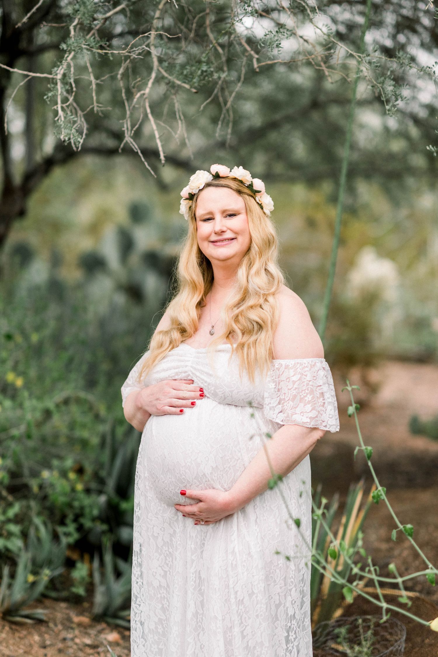 Ethereal maternity portrait in a garden with white lace dress and flower crown.
