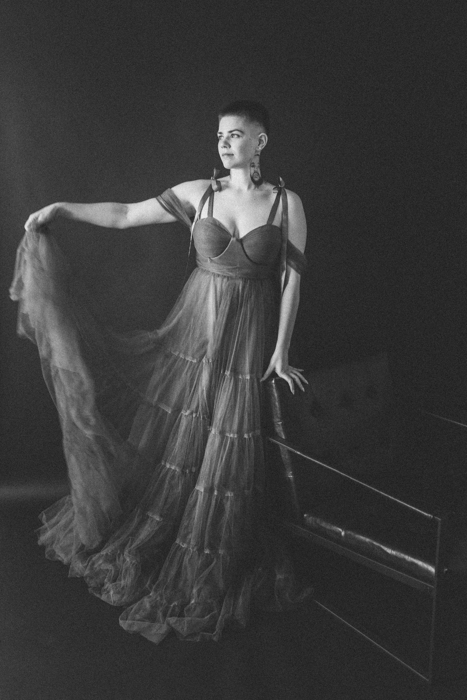 A black and white portrait of someone in a tiered tulle gown next to a modern bench.