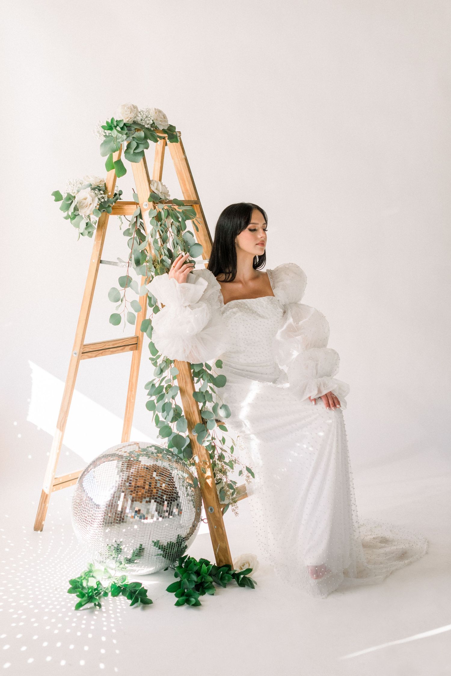 Decorative wooden ladder with greenery and disco ball in white studio setting.