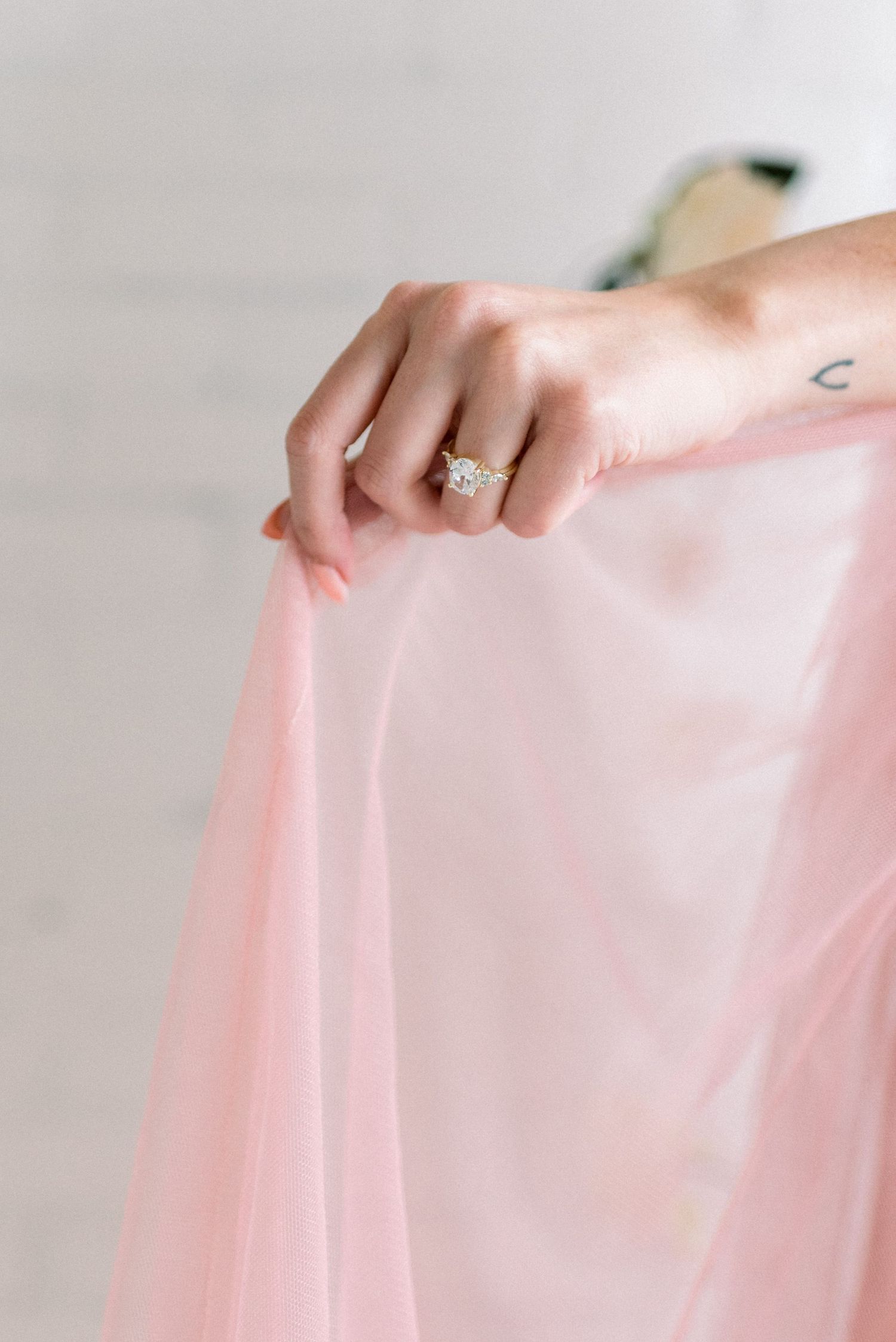 Close up of an engagement ring on a hand holding pink tulle fabric.