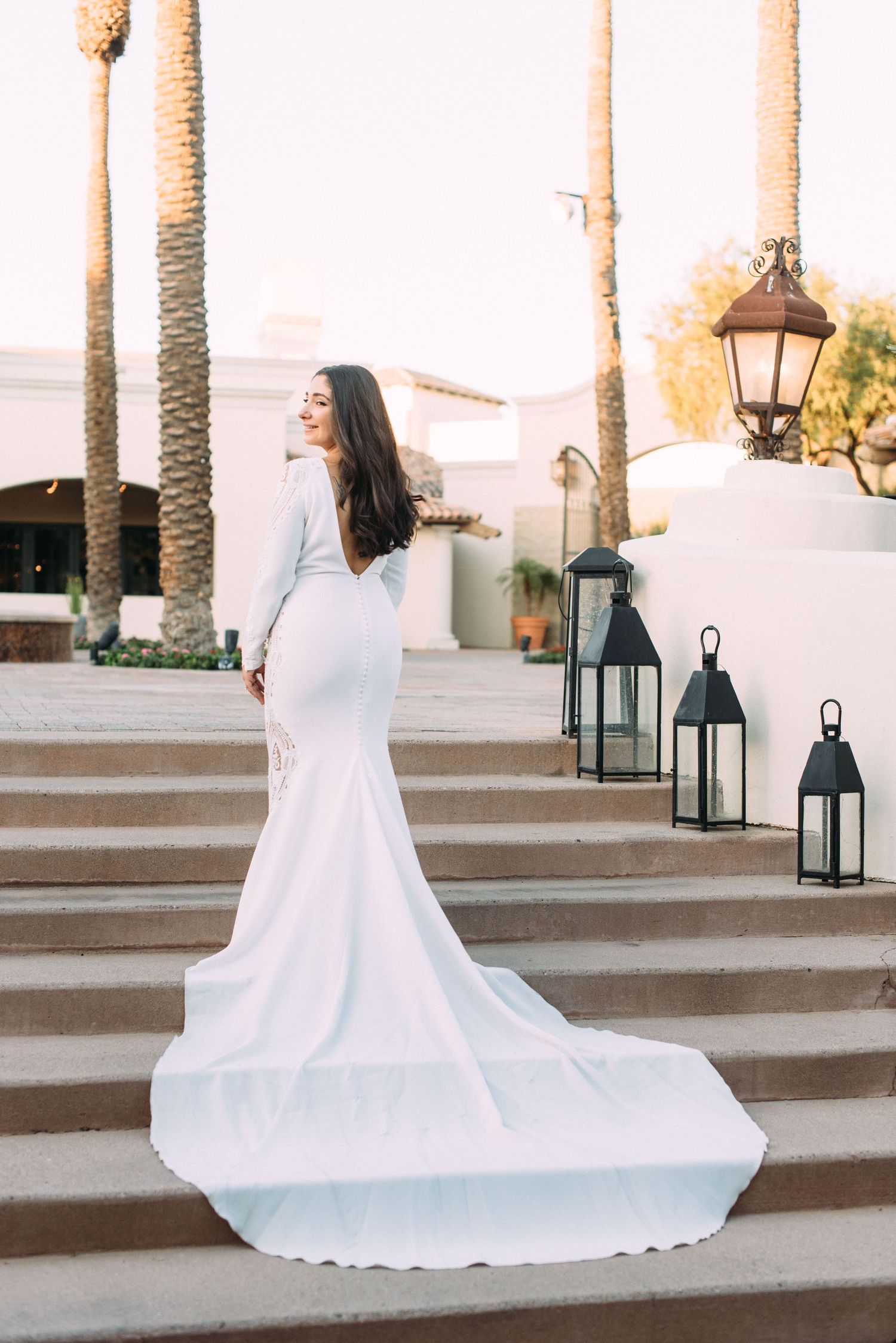 An elegant white wedding dress with a long train flows down stone steps adorned with lanterns.