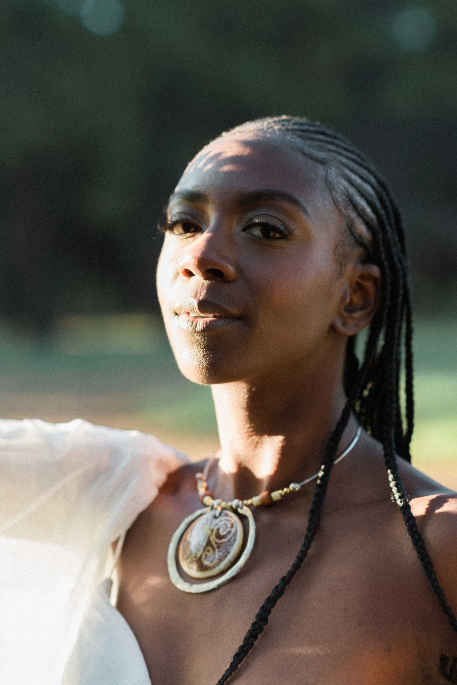 A close-up portrait of a bride wearing a statement shell necklace in golden sunlight.