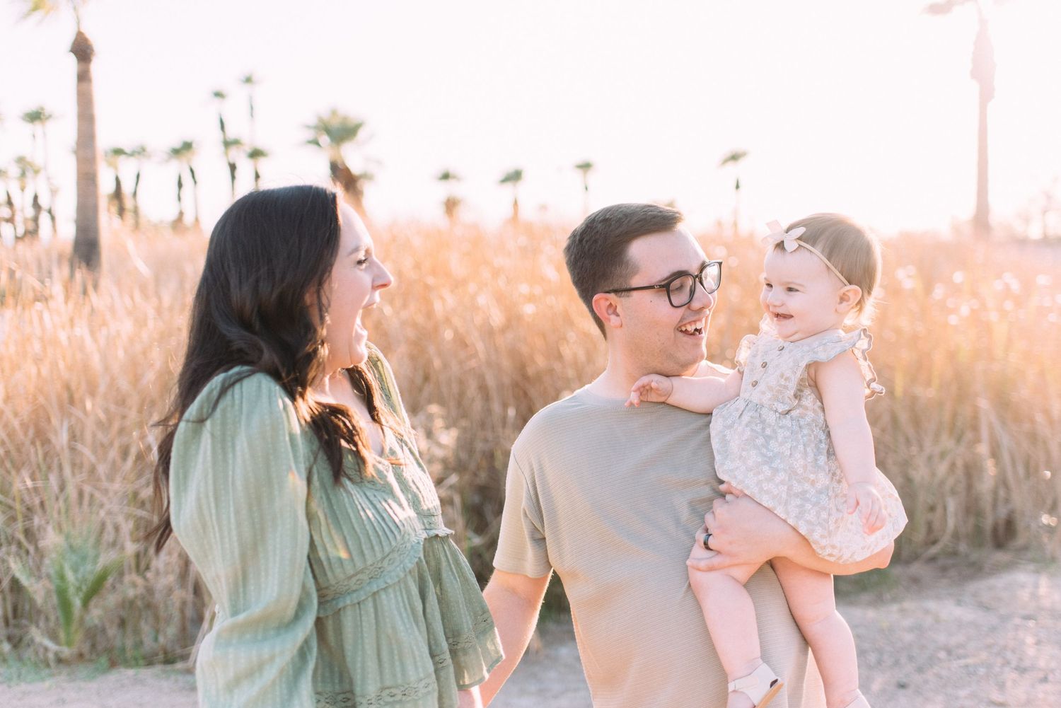 A happy family of three interacts warmly on a palm-lined path during golden hour.