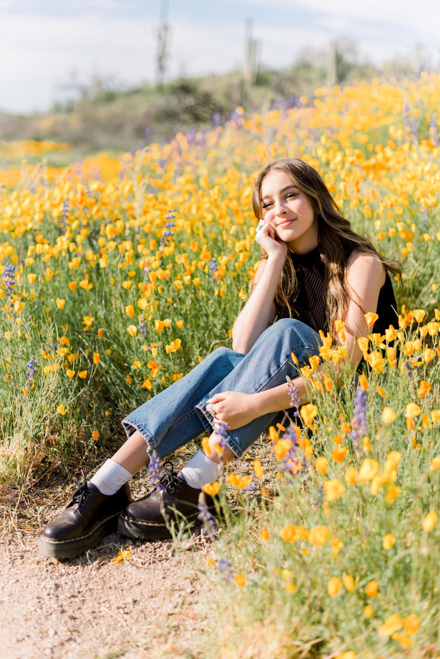 Relaxed outdoor portrait among yellow wildflowers wearing casual denim and boots.