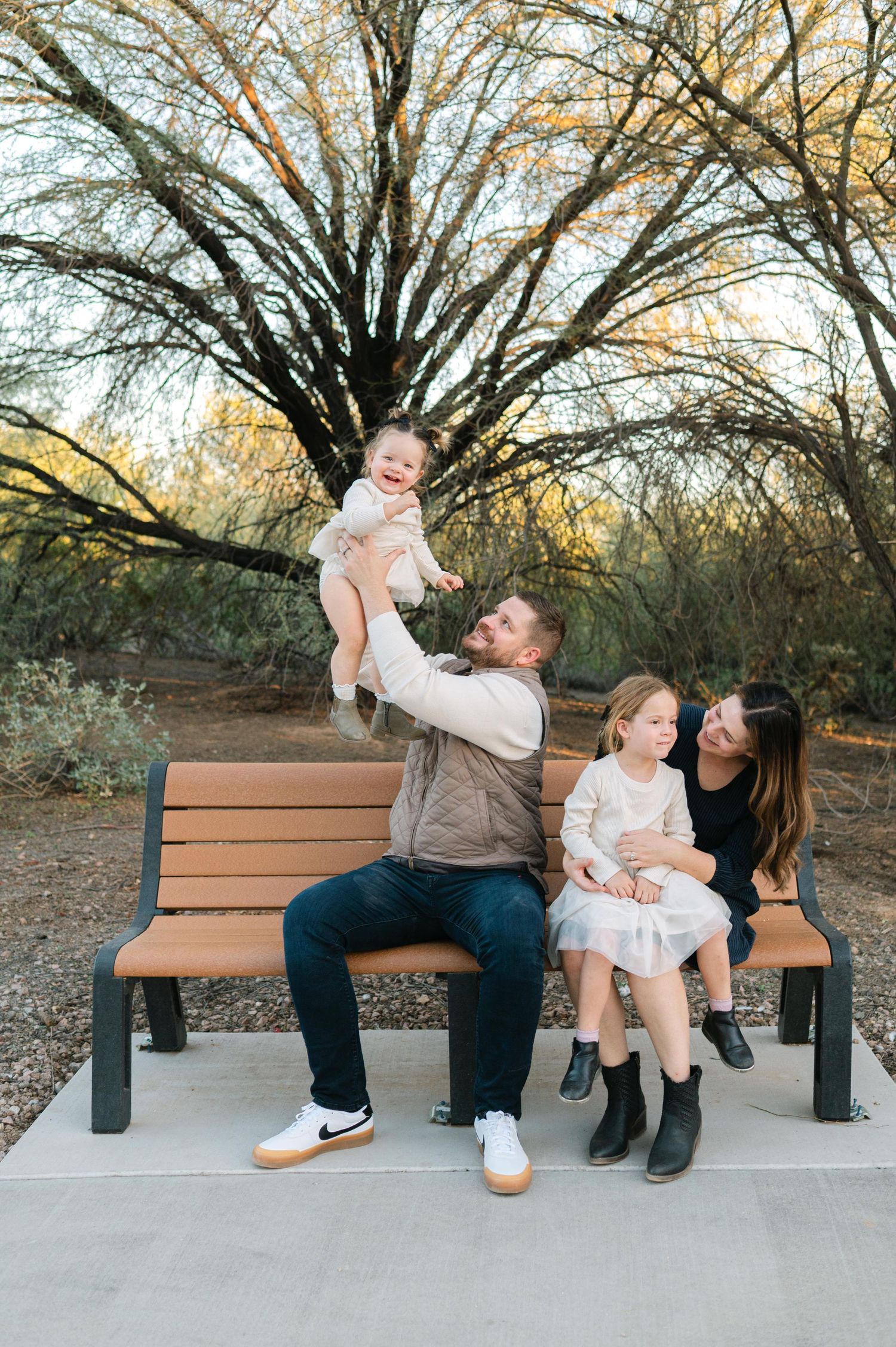 A family sharing playful moments together on a wooden bench in a park setting.