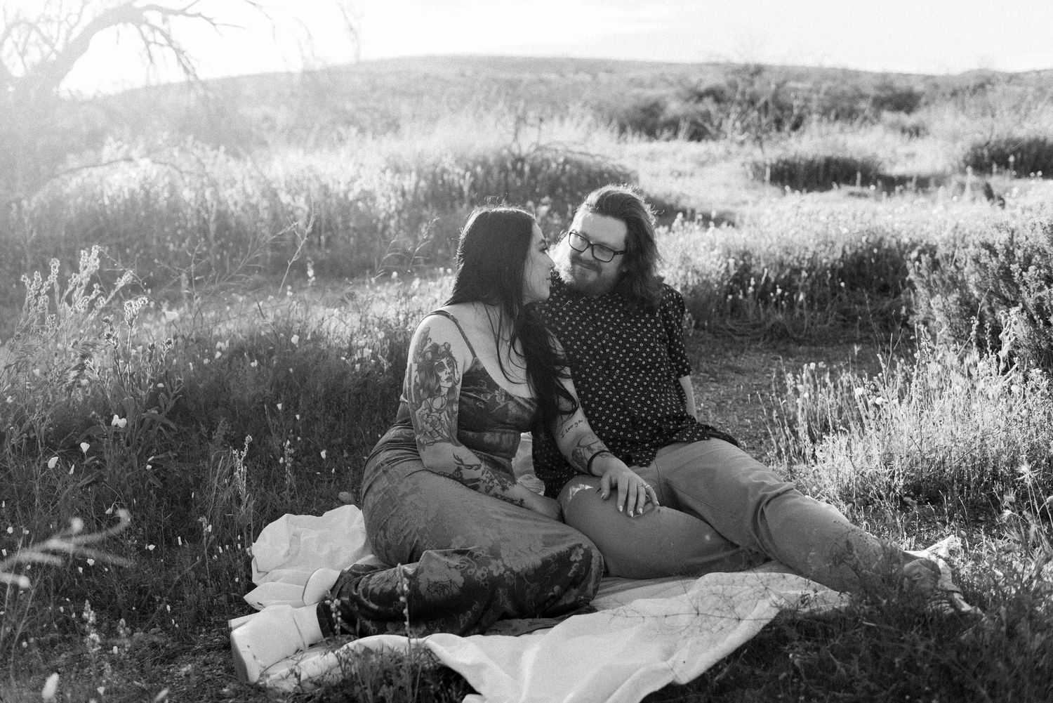 A couple lies together in a grassy meadow on a sunny afternoon, creating a romantic outdoor moment.