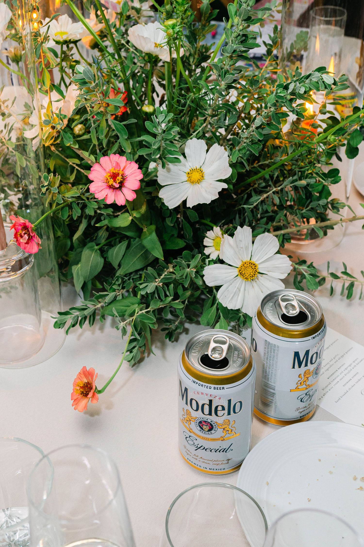 Fresh garden flowers and beer cans create a casual centerpiece arrangement on a white table.