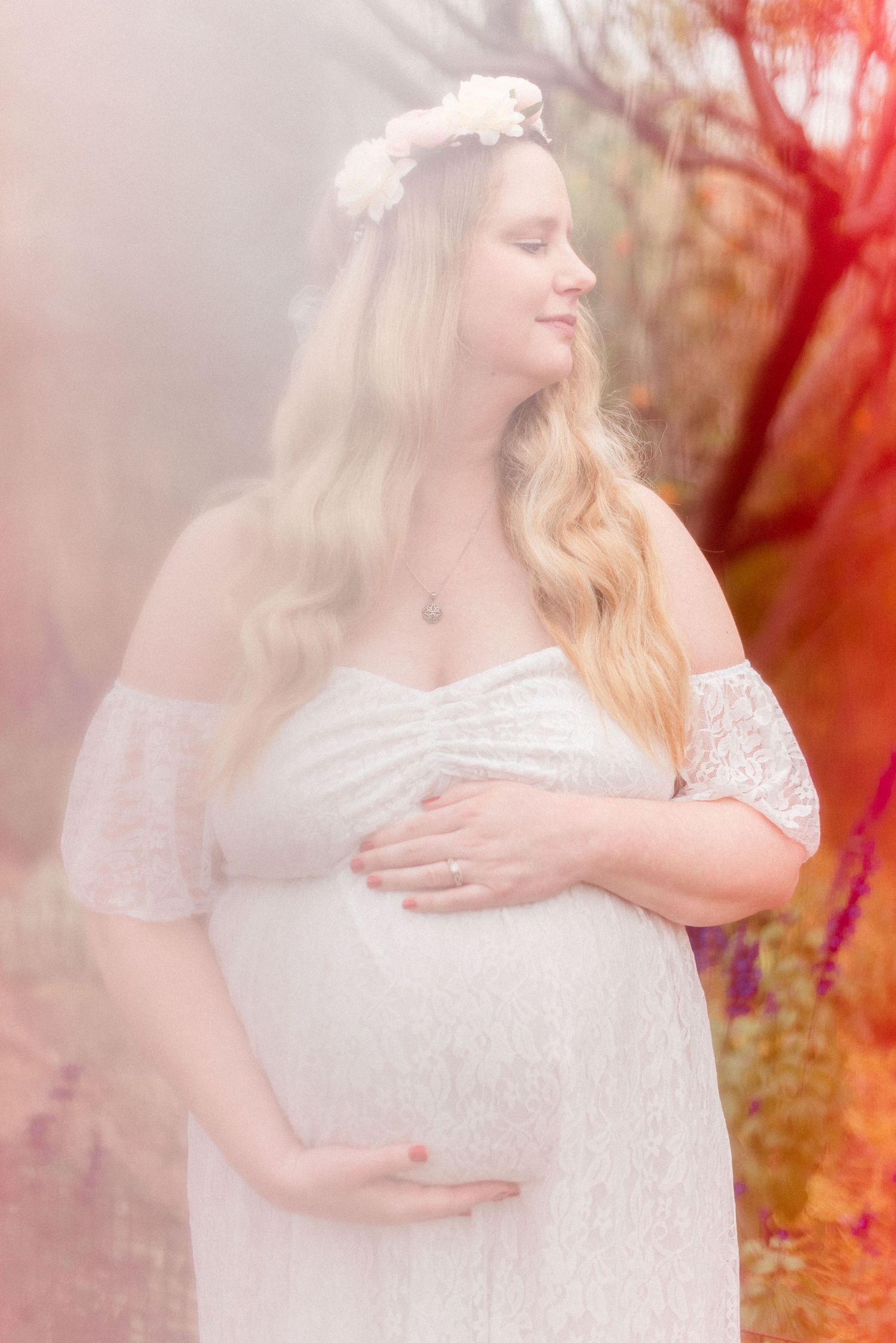 Dreamy maternity portrait with soft pink lighting and ethereal white dress.