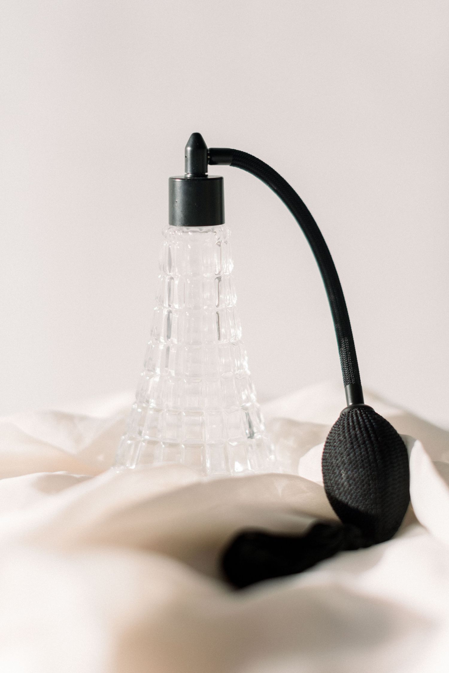 Vintage crystal perfume bottle with black atomizer on white fabric background.