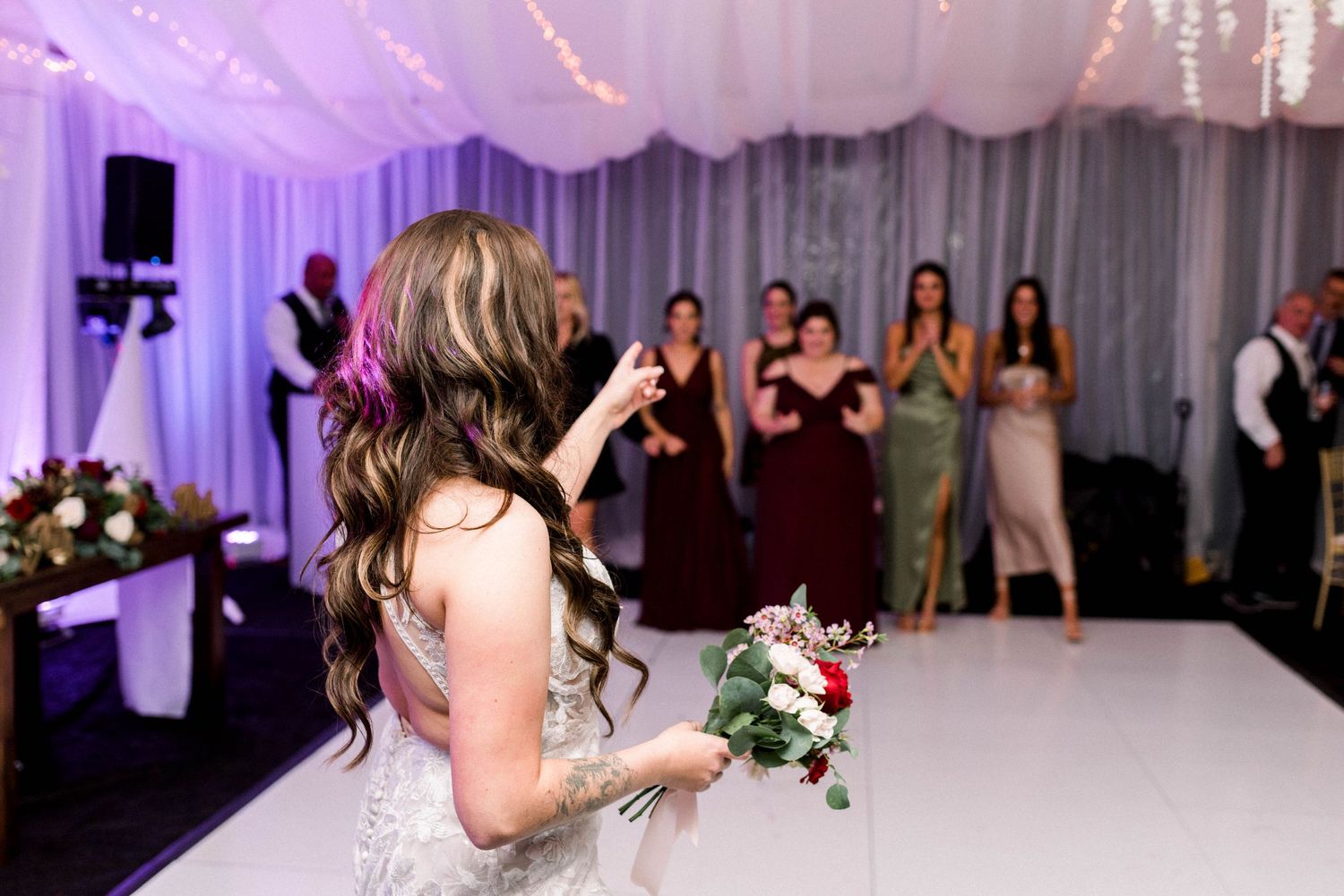 Bride preparing to toss her bouquet at wedding reception with guests watching in anticipation.