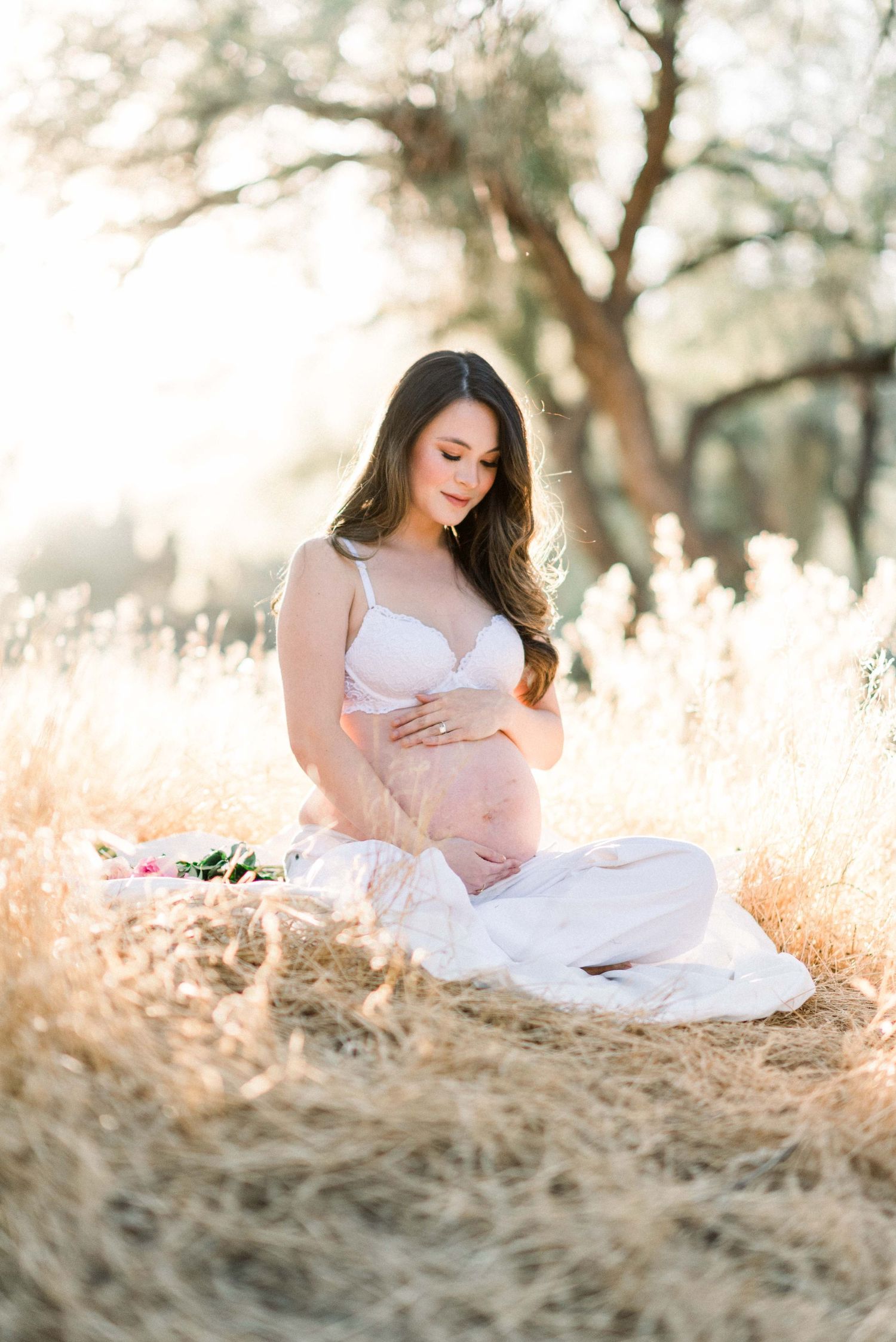 Intimate maternity portrait in white outfit sitting in golden grass field.