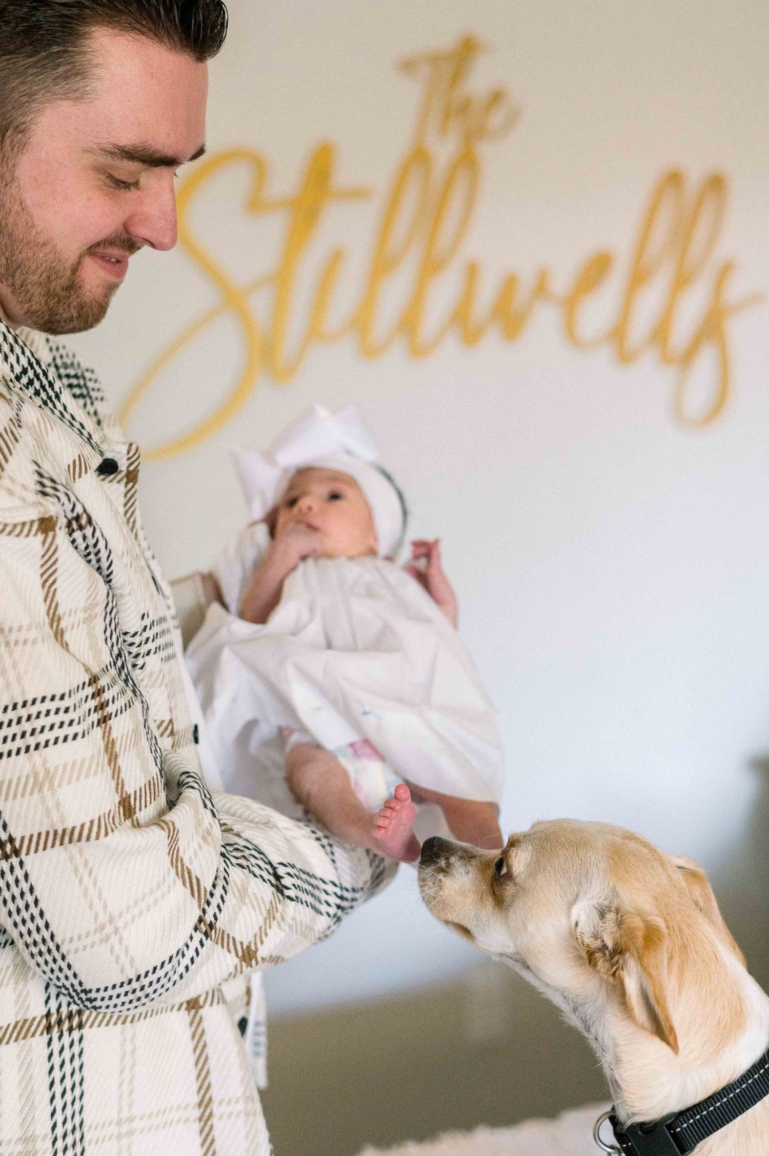 Family introduces newborn baby to their pet dog beneath gold wall lettering.