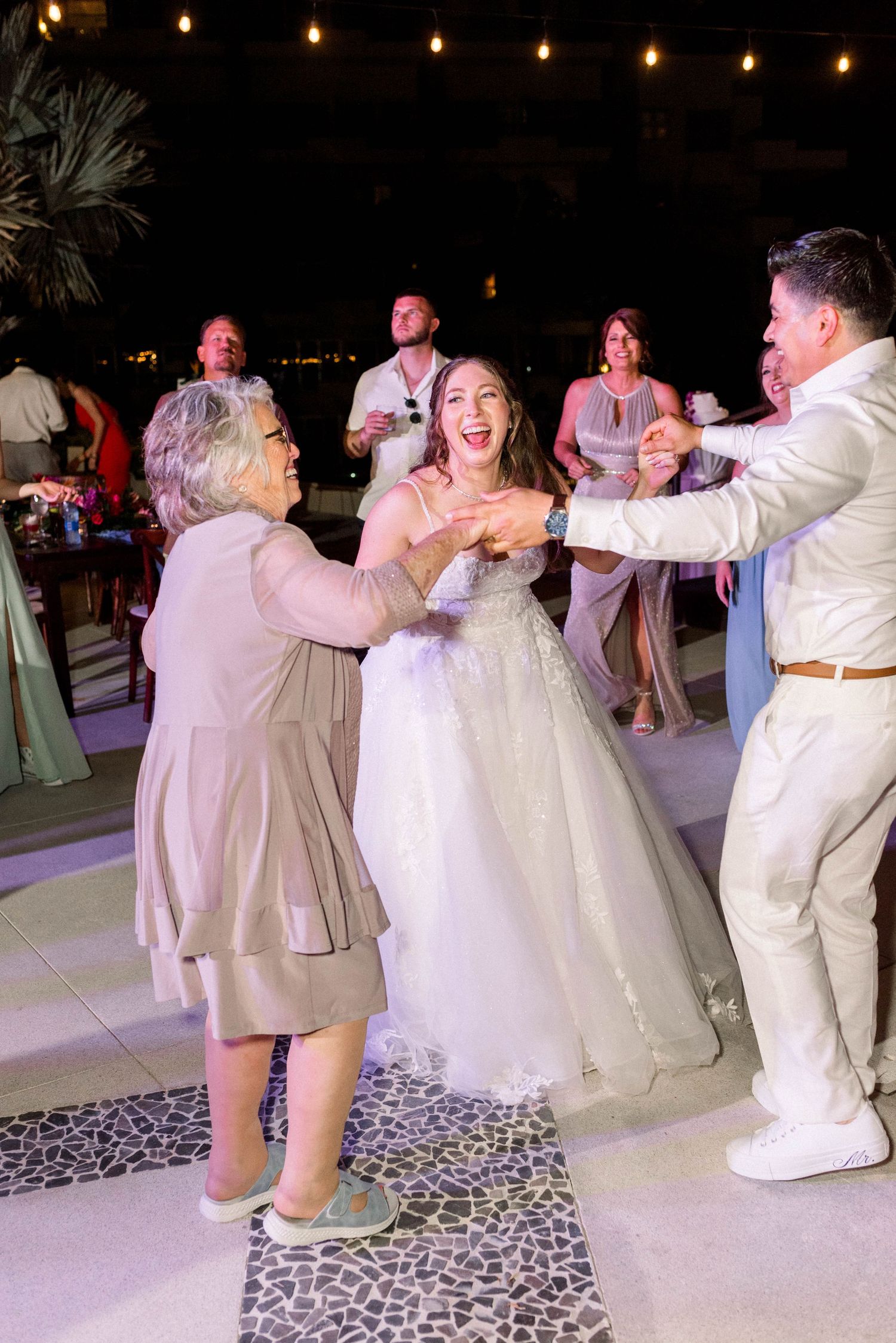 Wedding guests dancing joyfully with the bride at an outdoor evening reception.