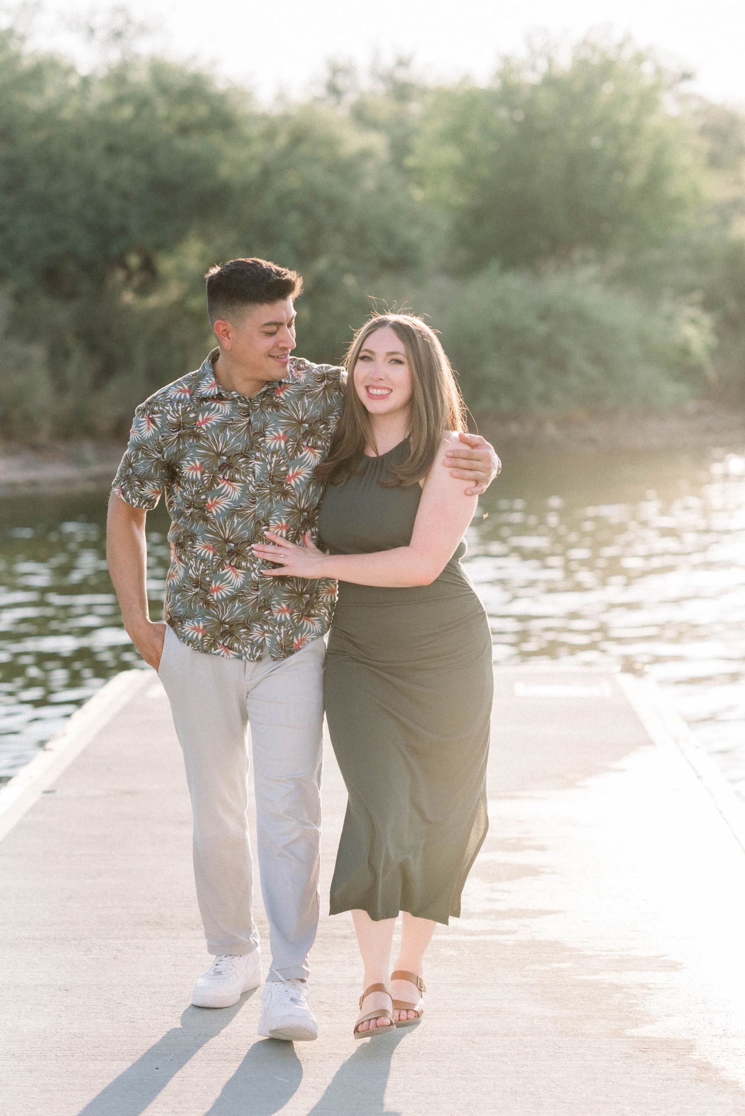 A romantic couple in casual attire walking together on a waterfront pathway.