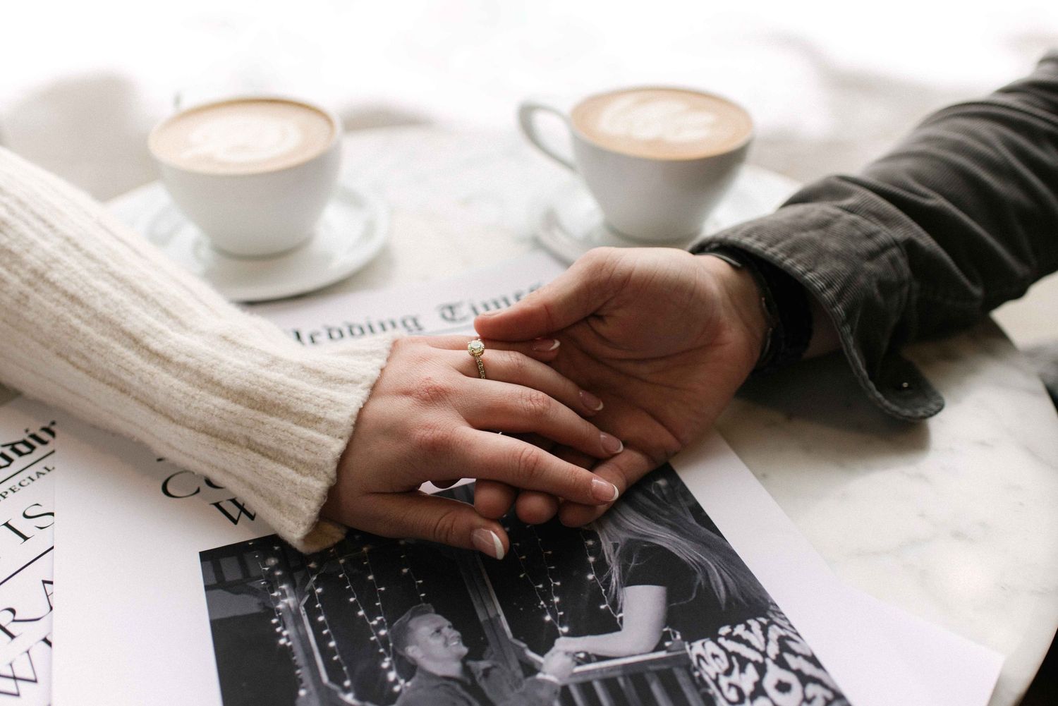 Hands clasped together on a table with coffee cups and newspaper in the background.