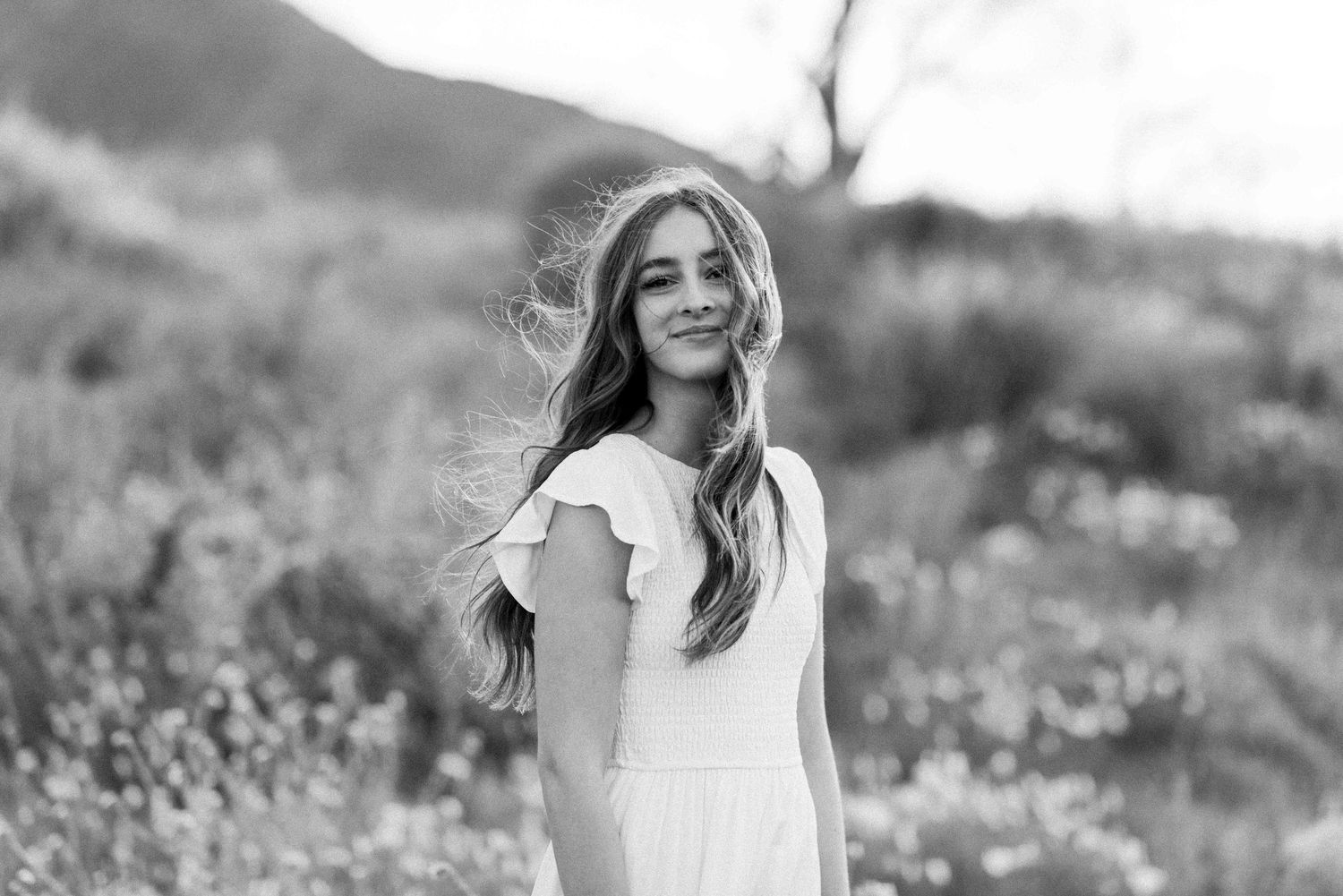 Black and white portrait showing natural joy in outdoor wildflower setting.