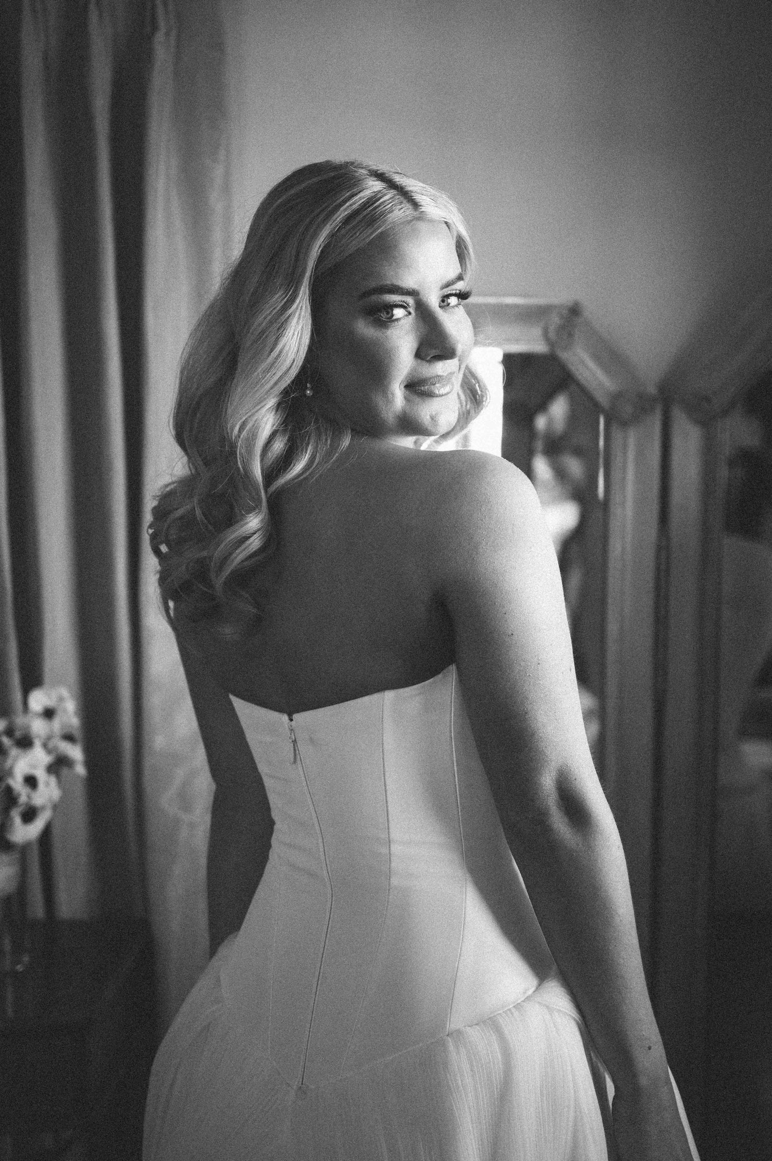 Black and white portrait of bride in strapless wedding dress looking over her shoulder.