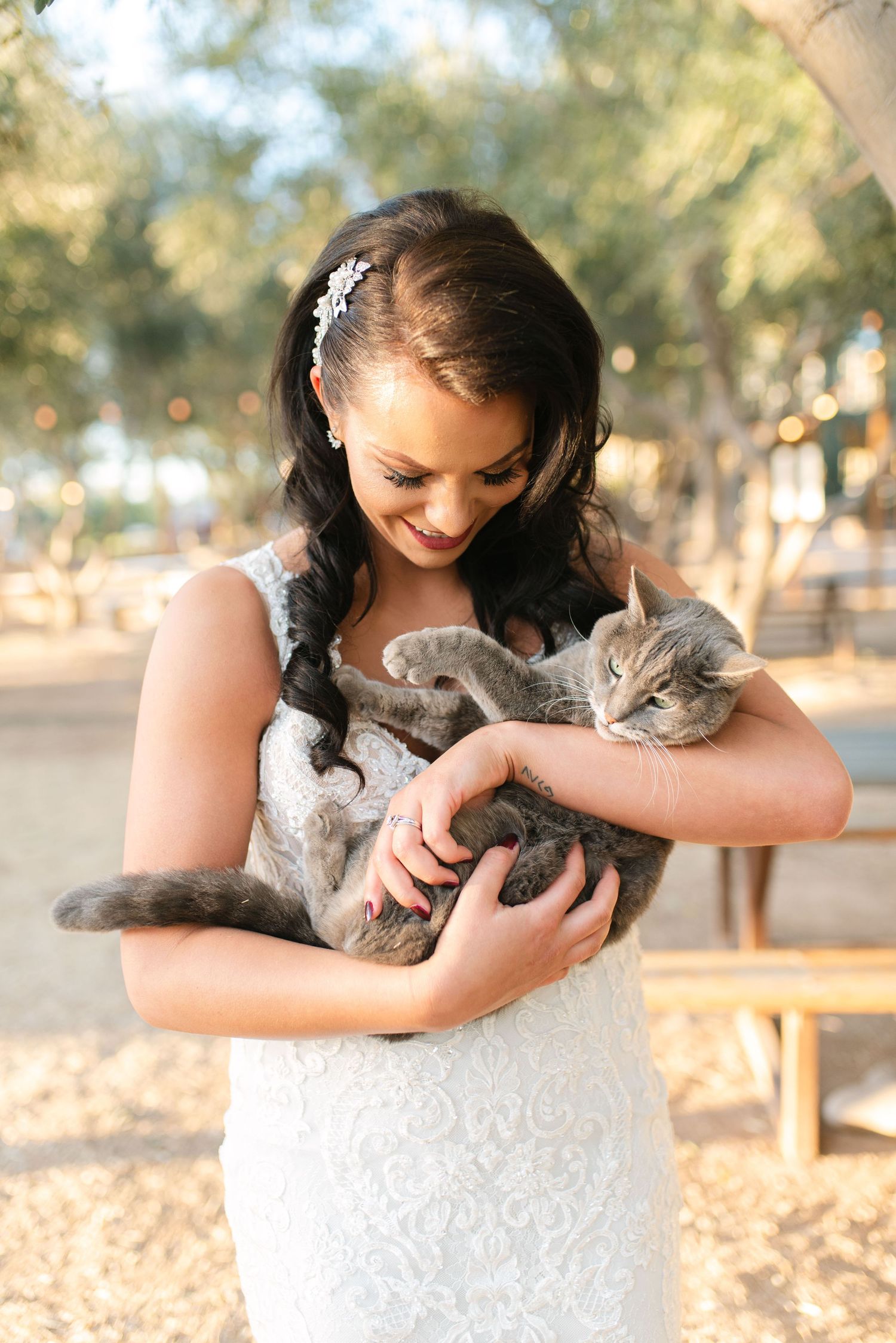 Sweet moment between a bride in white lace dress and gray cat in outdoor setting.