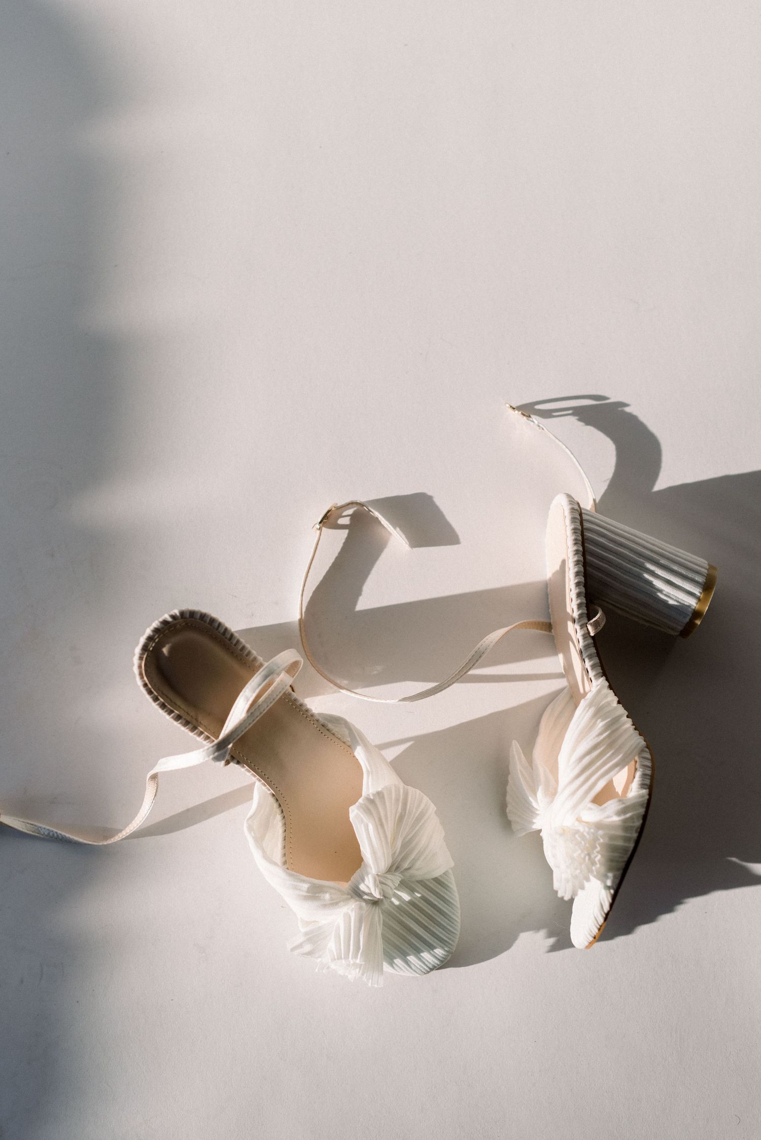 Elegant white bridal shoes casting dramatic shadows in natural light.