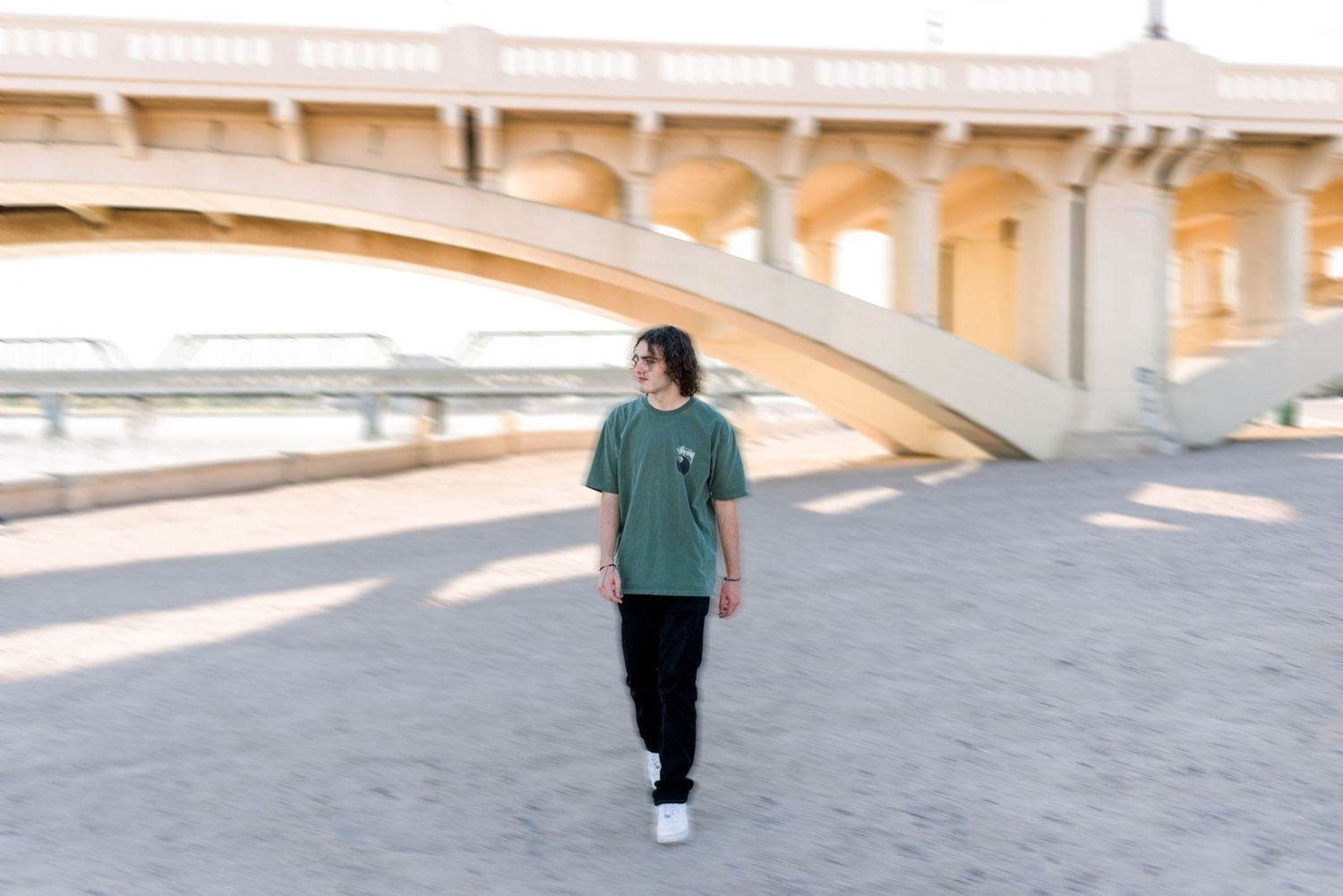 Person in green t-shirt walking under architectural bridge structure.