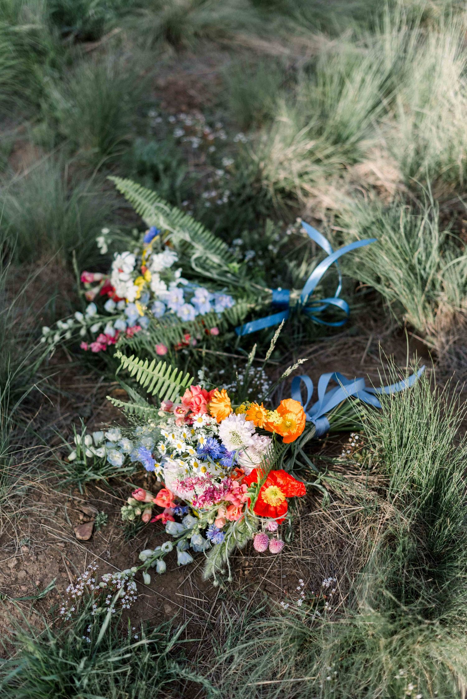 Colorful wedding bouquets with wildflowers and blue ribbons lying on grassy ground in natural outdoor setting.