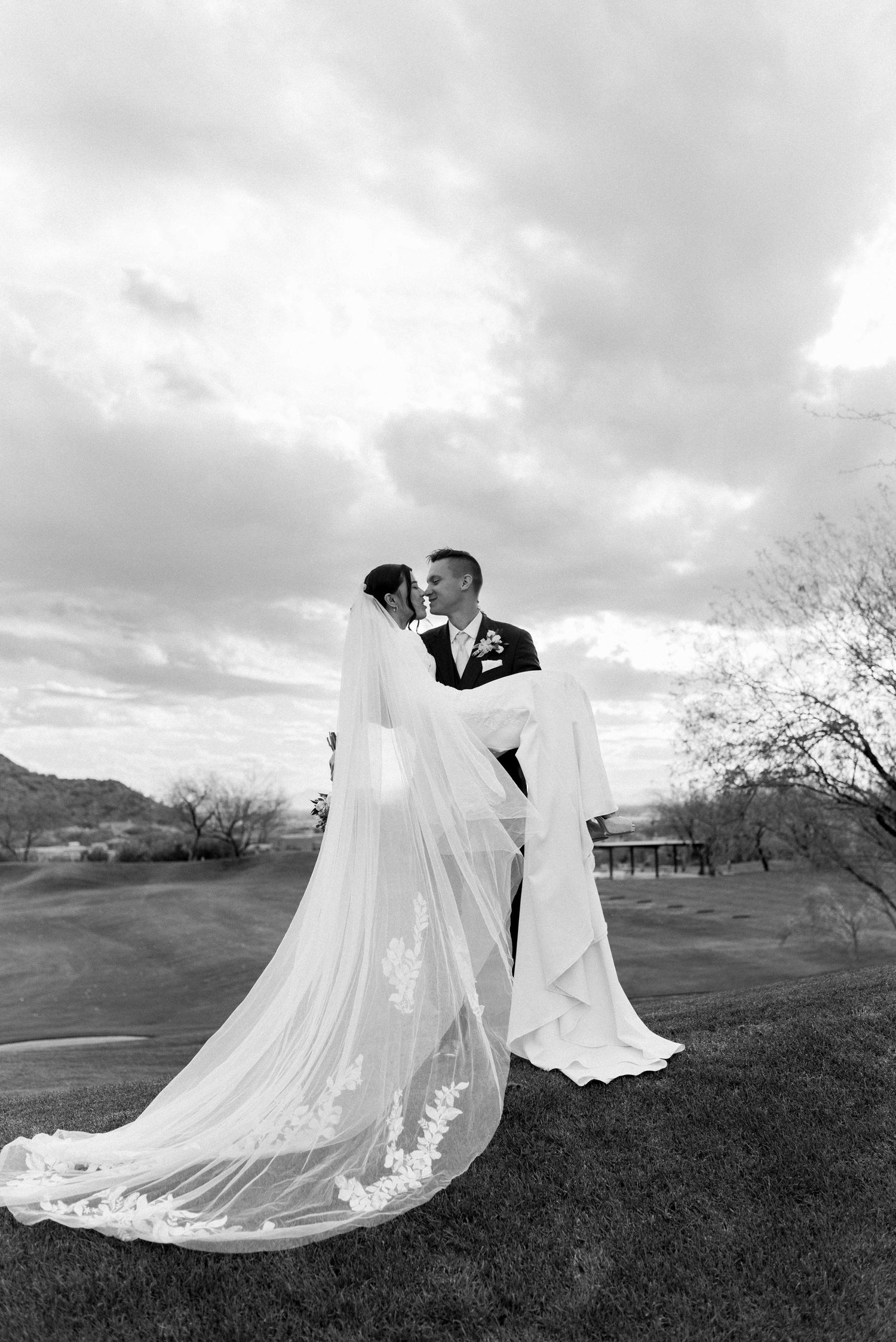 Dramatic black and white wedding photos with flowing veil against mountain backdrop.
