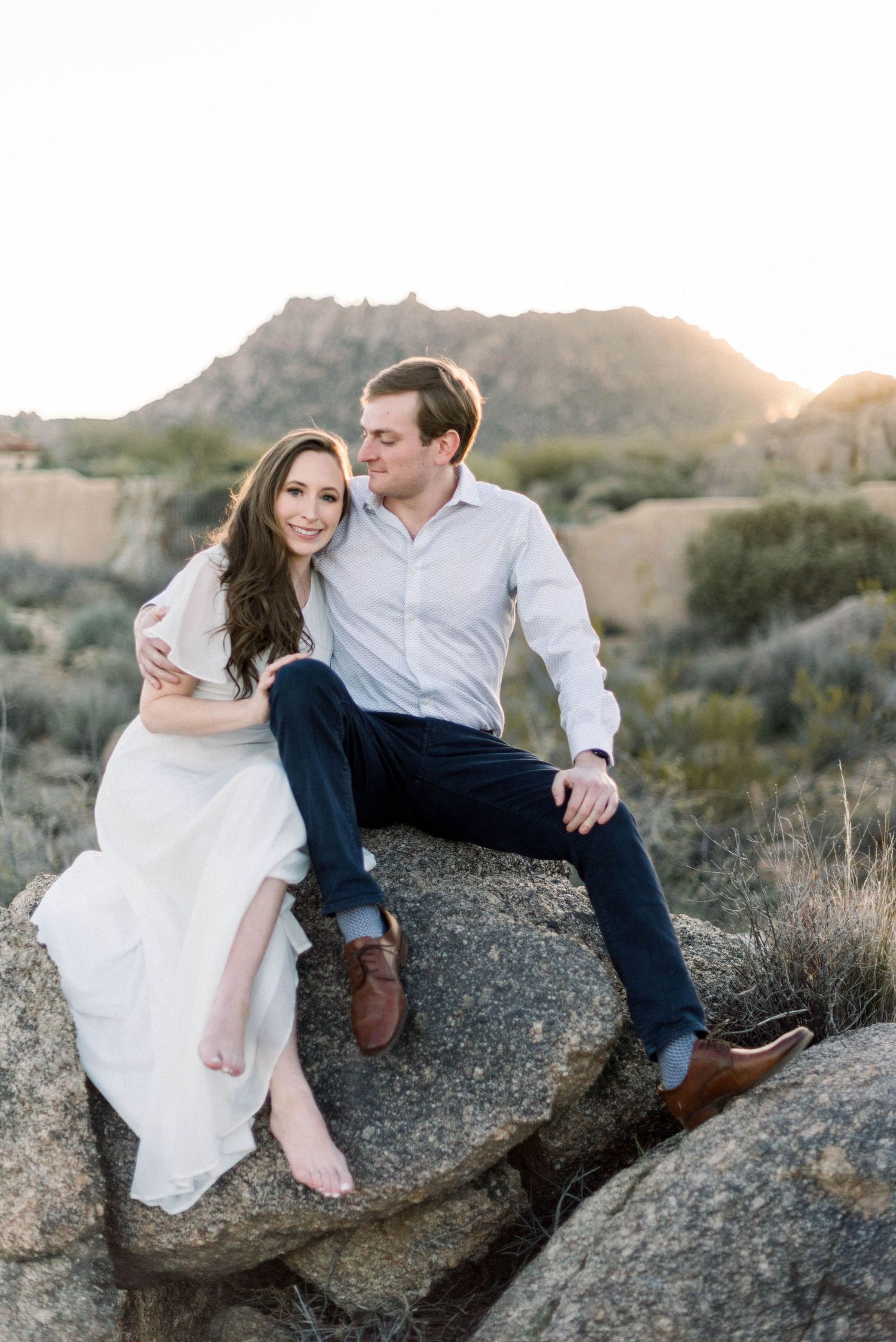 Couple shares tender moment while sitting on desert rock formation at sunset.