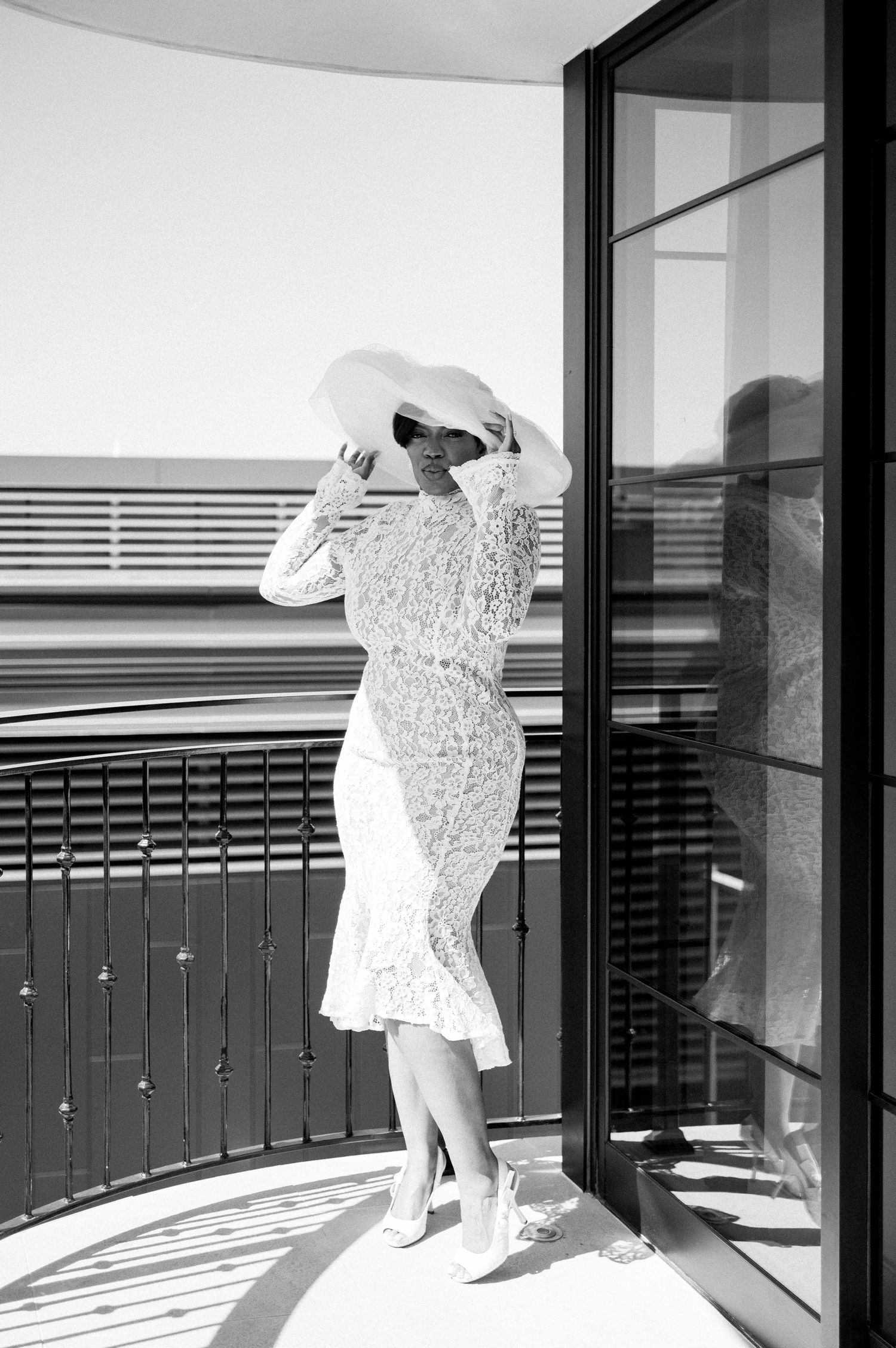 A sequence of black and white photos showing a figure in white moving across a modern balcony with glass panels.