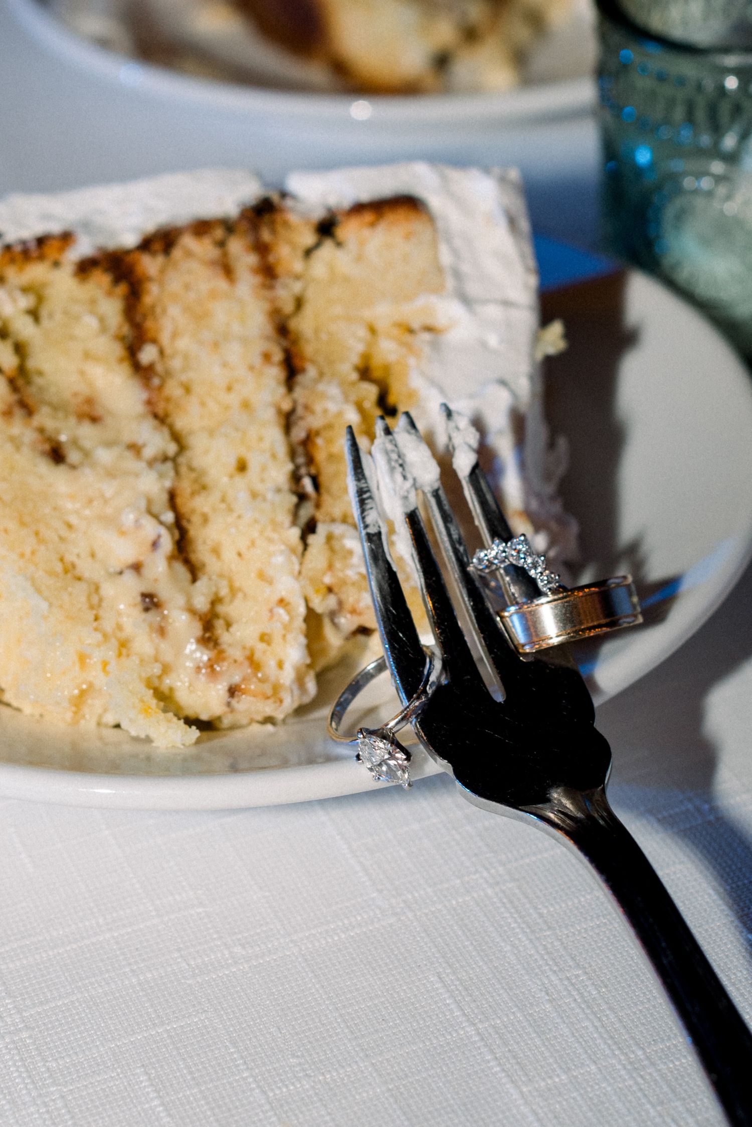 Close-up of wedding rings balanced on a fork next to a slice of vanilla wedding cake.