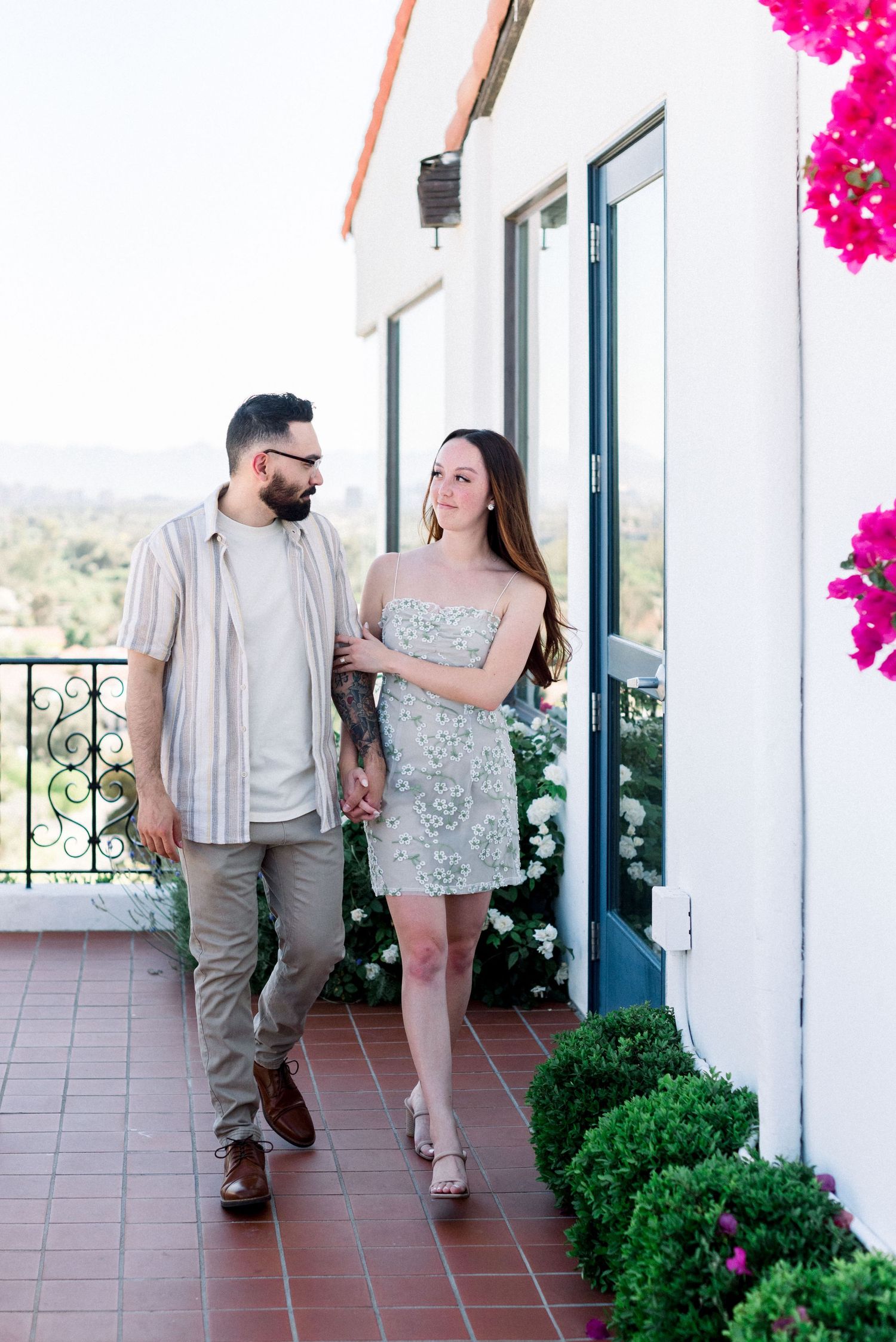 Couple walking together on Mediterranean style terrace with pink bougainvillea flowers.