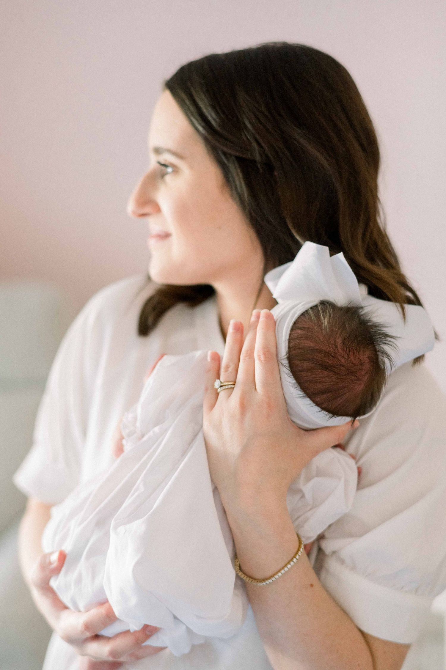 Side profile of parent holding sleeping newborn against pink wall background.