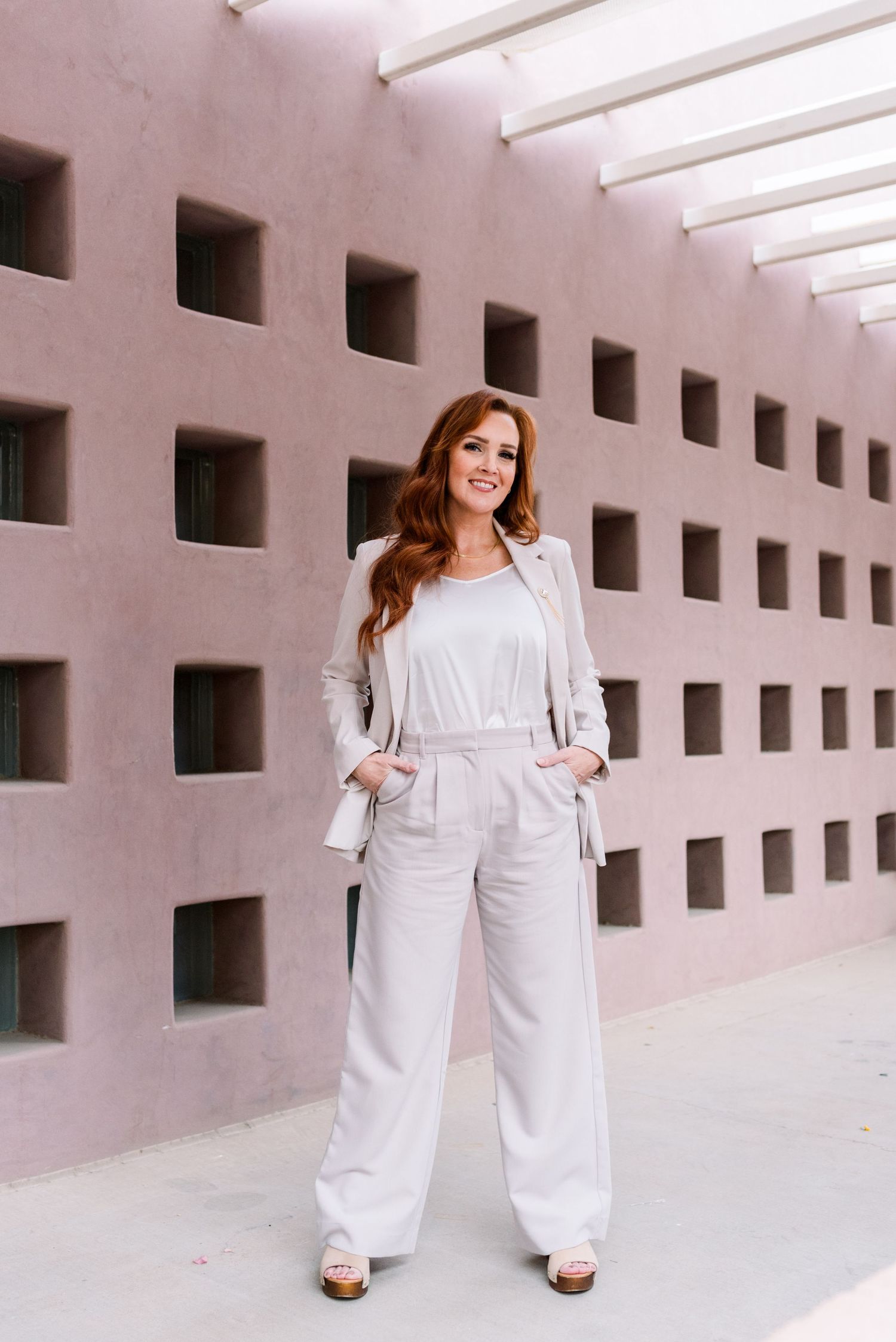 Person in all-white ensemble poses in front of geometric wall pattern with dramatic lighting.
