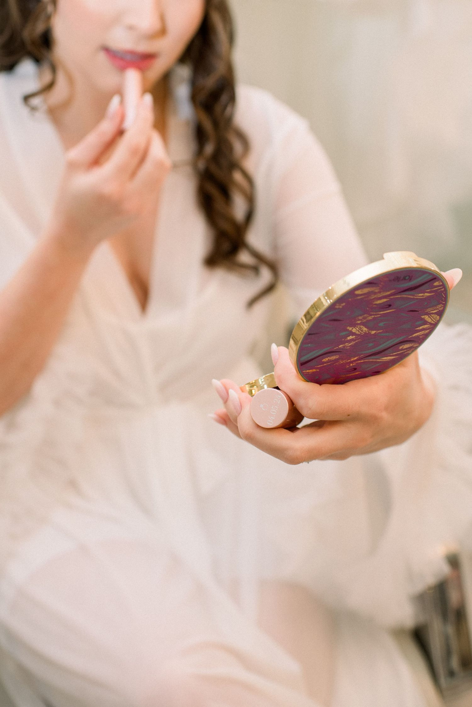Hand holding a vintage-style compact mirror while getting ready in a white robe.