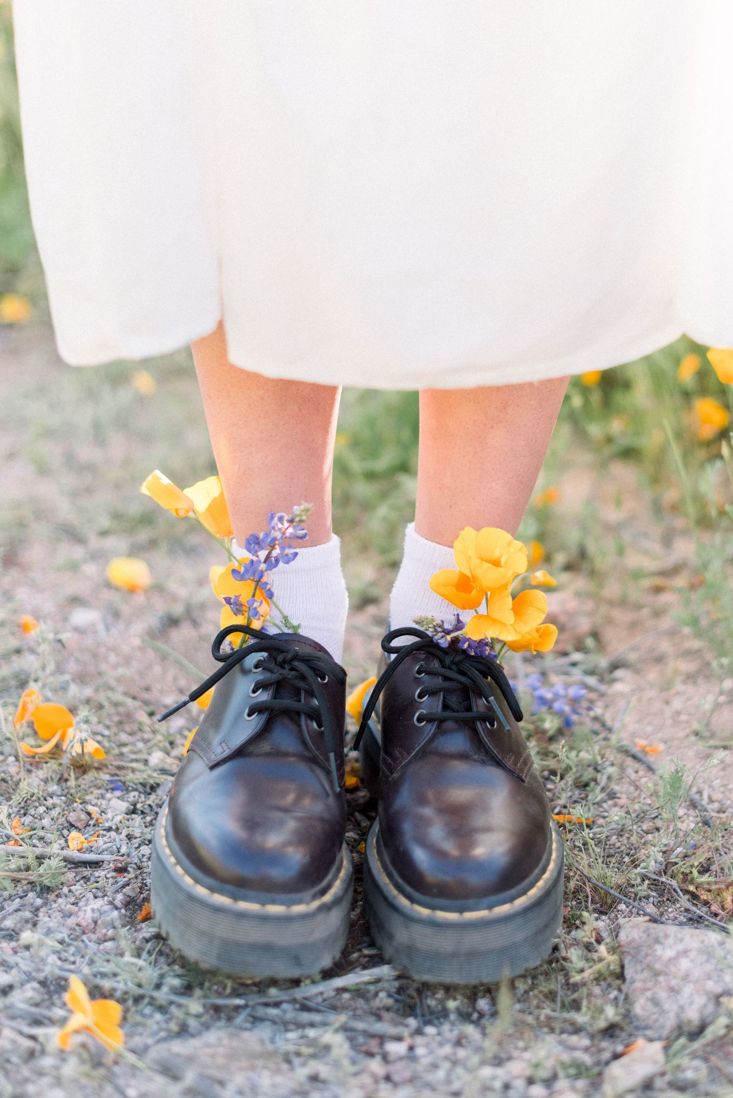 Black platform shoes adorned with yellow flowers against white dress hem and scattered petals.