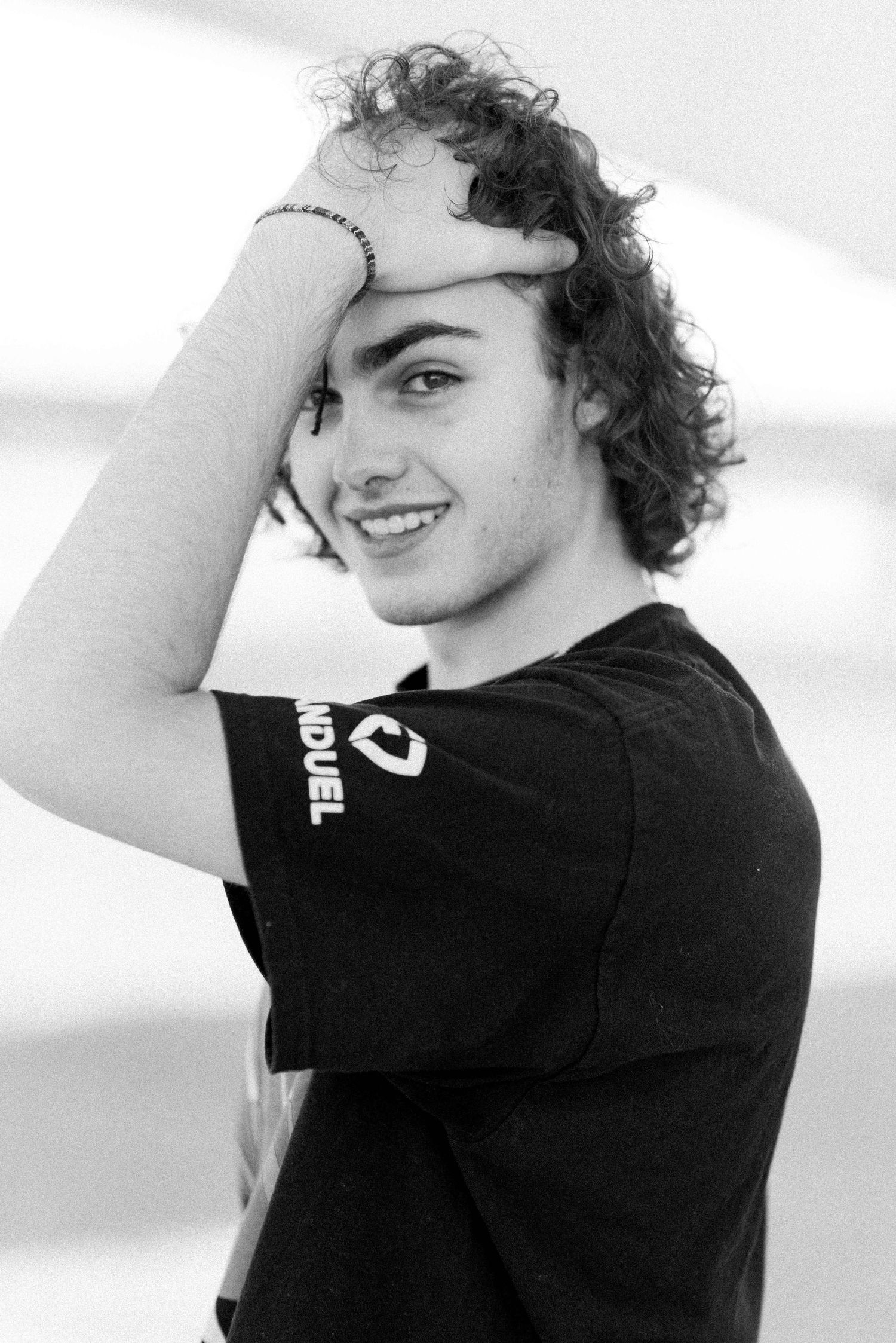 Black and white portrait of person with curly hair and black t-shirt.