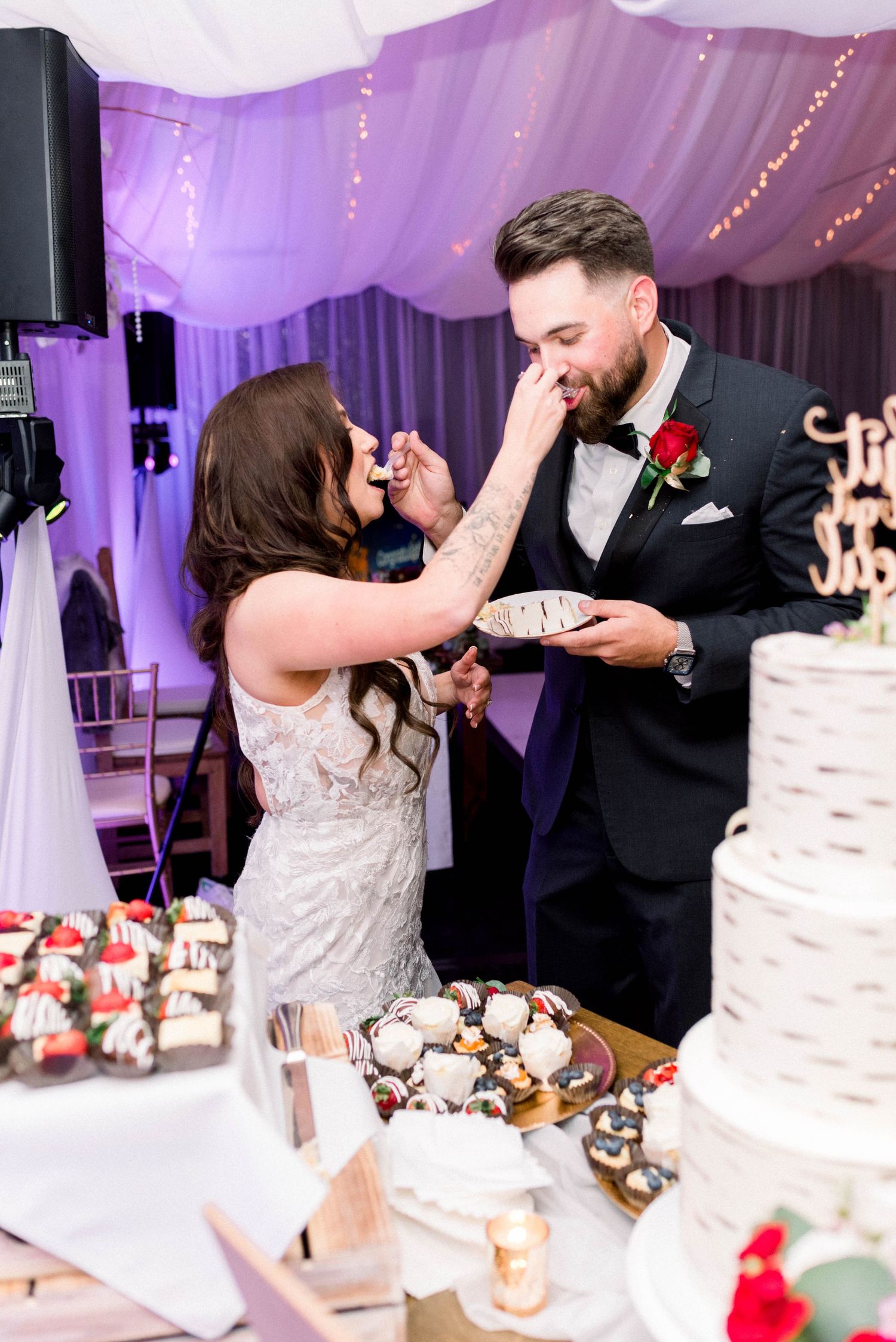 Couple playfully feeds each other wedding cake during traditional cake cutting ceremony.
