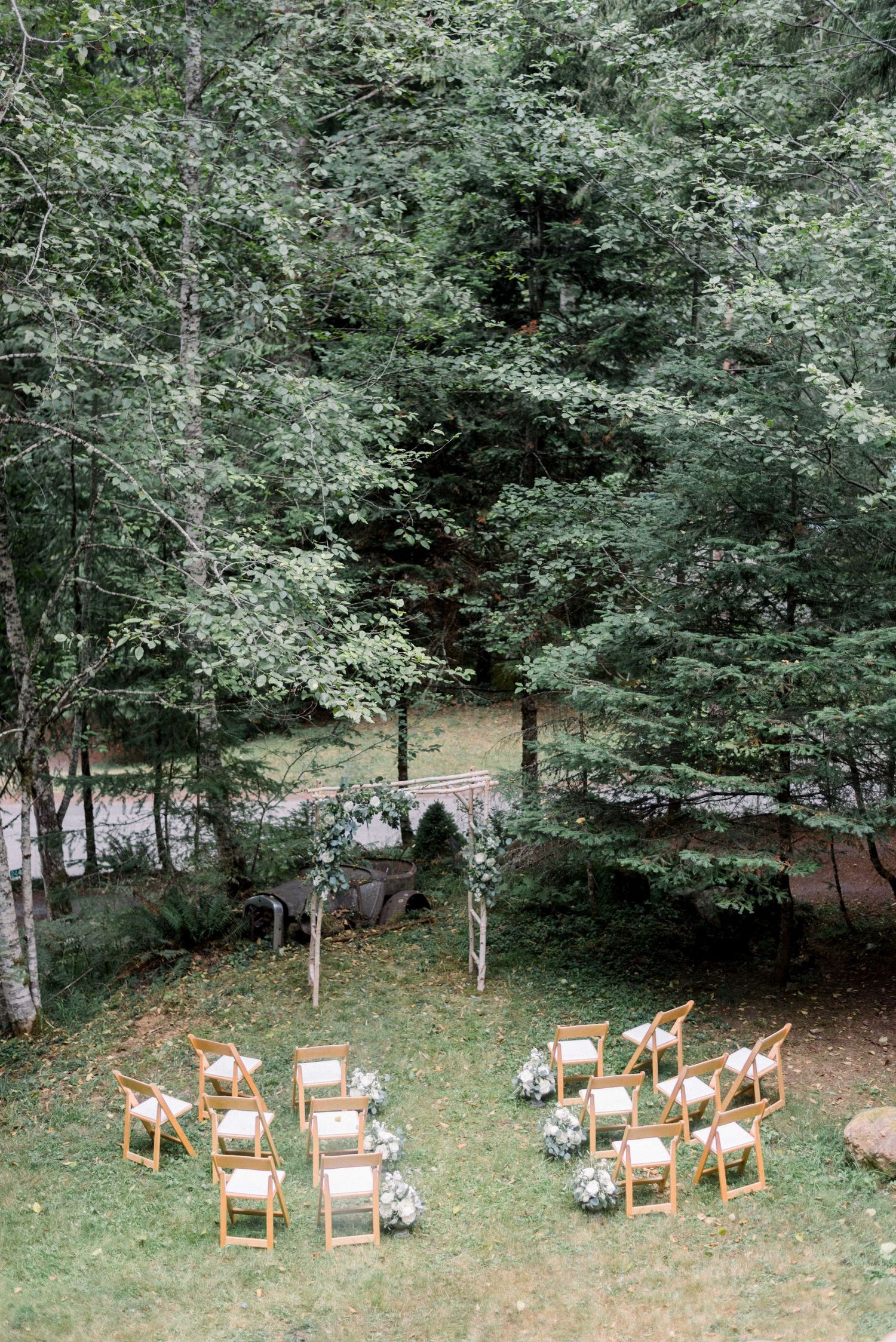 An intimate woodland wedding ceremony setup with wooden chairs and floral arrangements.