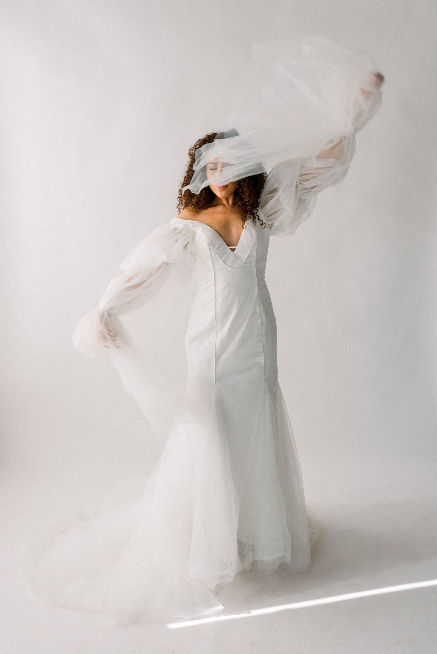 Artistic bridal portrait with flowing veil movement against white background.